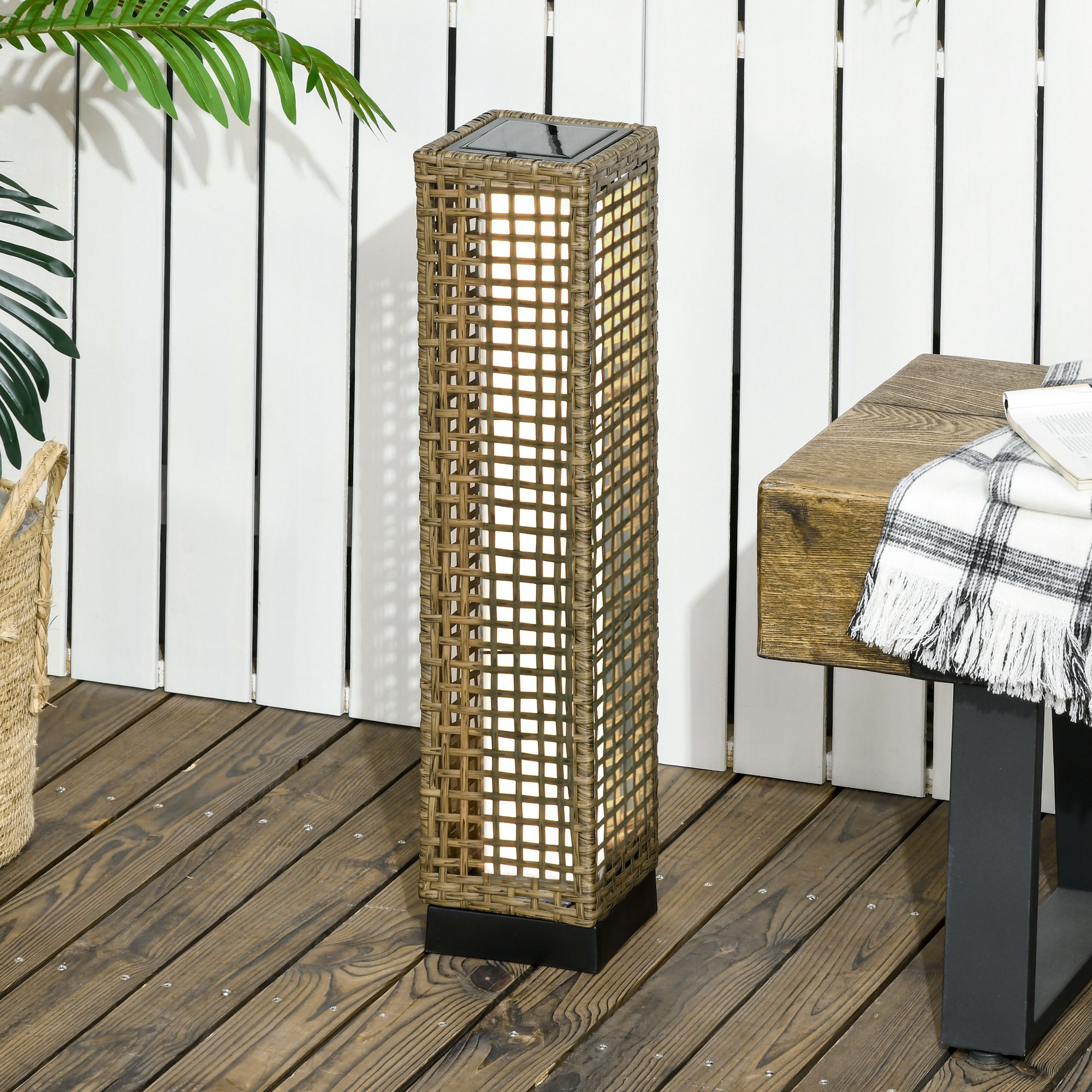 Una luce solare rettangolare in stile rattan su un ponte di legno. Un tavolo e delle piante sono vicini.