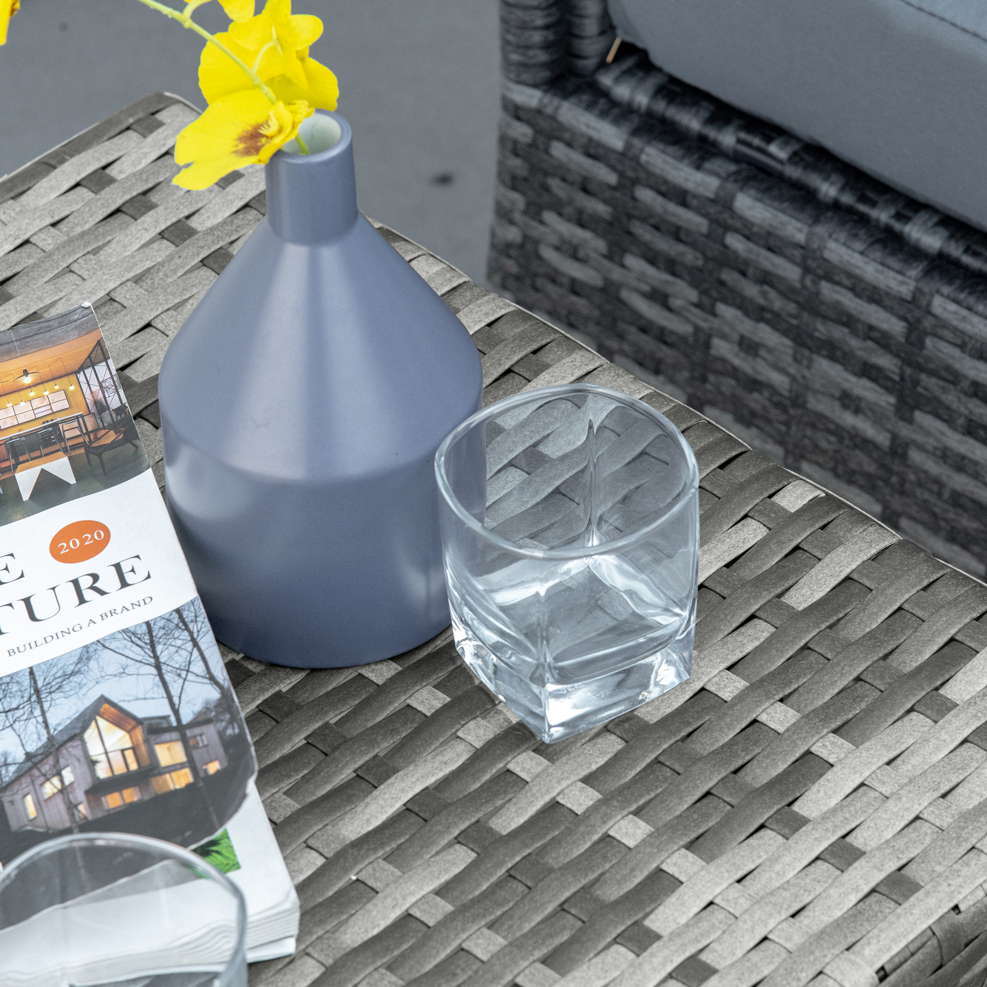 Un tavolo grigio intrecciato con un vaso, fiori e una rivista sopra.