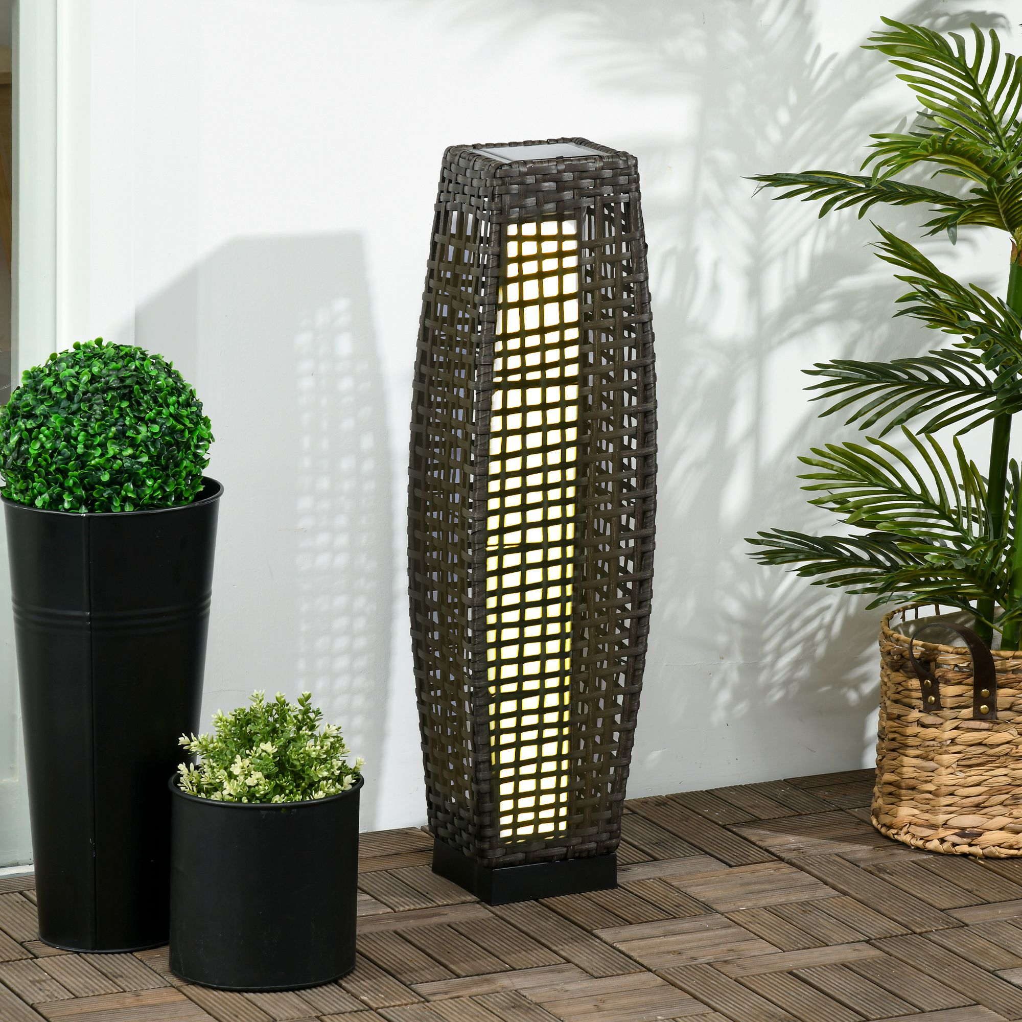 Una lampada alta da esterno con paralume marrone intrecciato. Piante in vaso. Terrazza in legno.