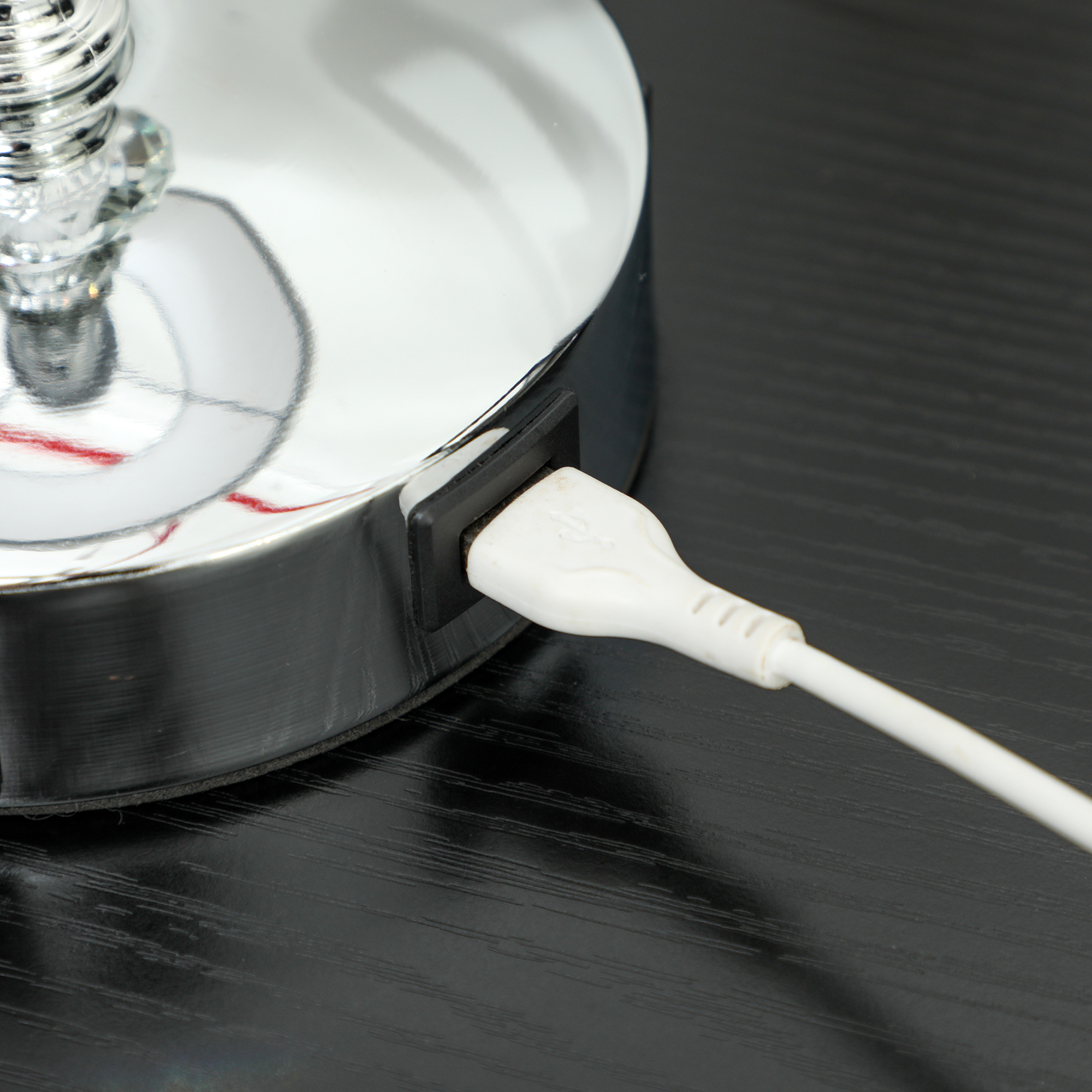 Un primo piano di una base di lampada argentata con una porta USB e un cavo bianco collegato.