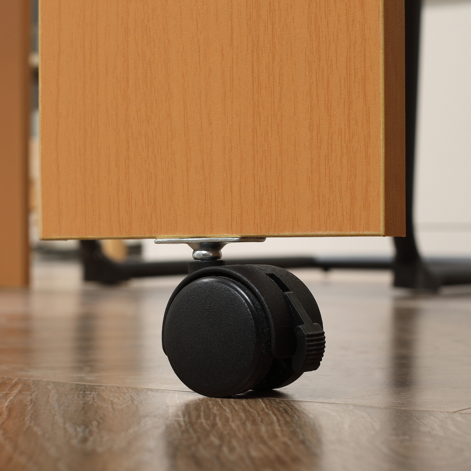 Primo piano di una ruota di un mobile nero. Sotto una superficie in legno, su un pavimento in legno.