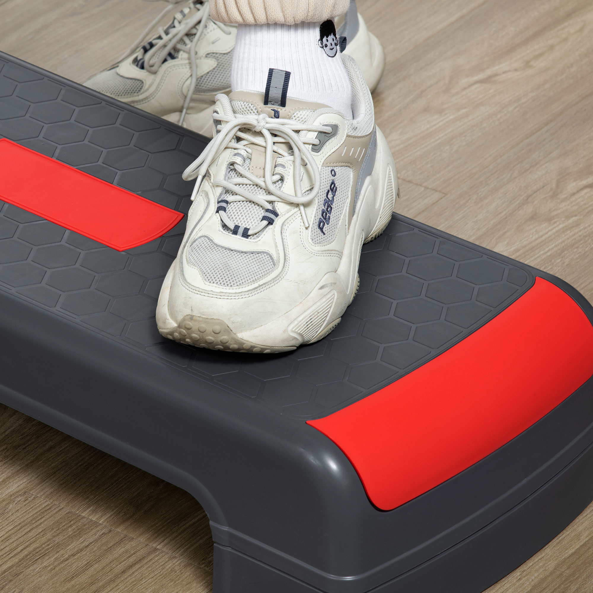 Piedi di una persona su una piattaforma di step grigia e rossa, con scarpe da ginnastica.