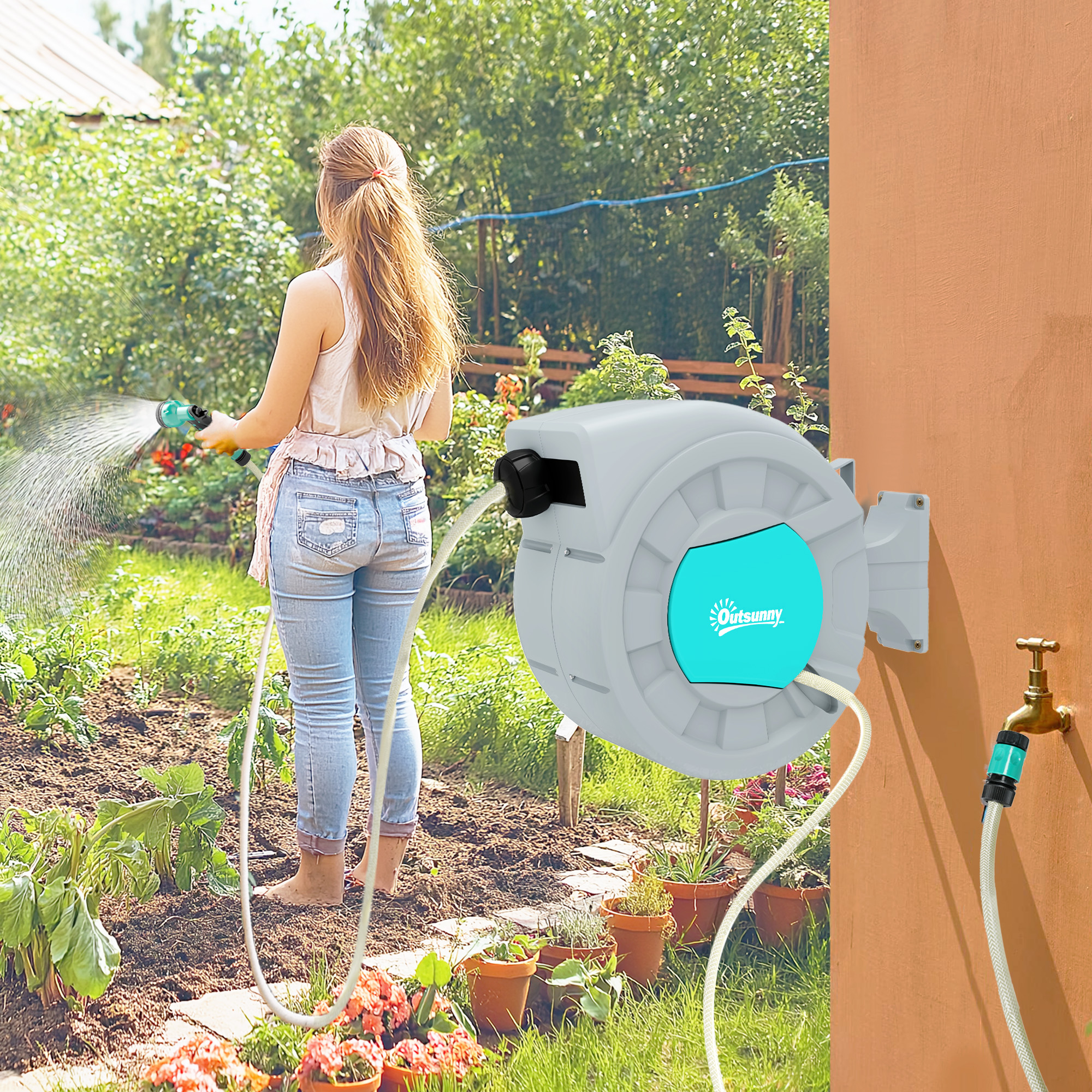 Una donna sta innaffiando un giardino. Sta usando un tubo con un avvolgitore grigio attaccato a un muro.