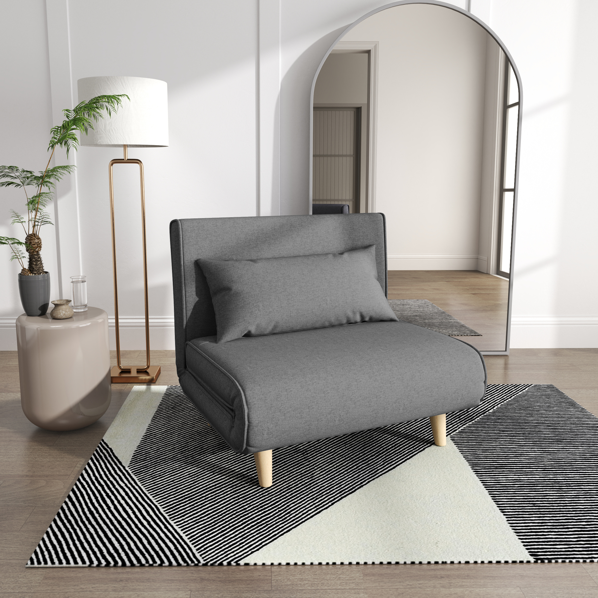 Un divano letto grigio con un cuscino e un tappeto a motivi bianchi e neri davanti. Lampada e specchio presenti.