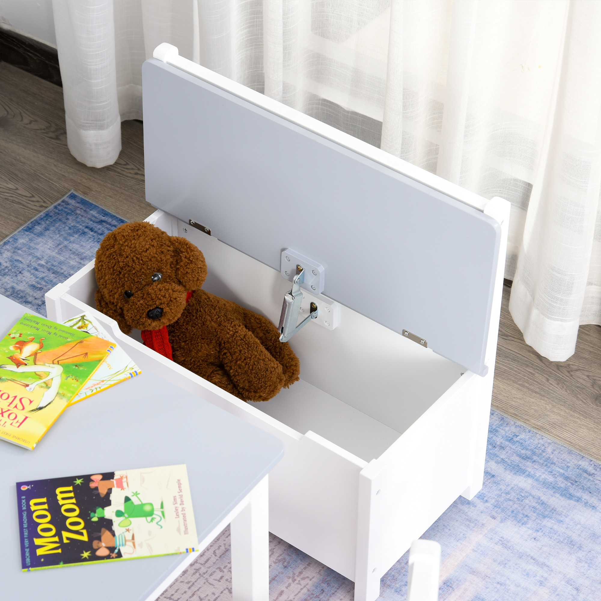 Un contenitore per giocattoli bianco con coperchio aperto. Un orsacchiotto e libri sono all'interno.
