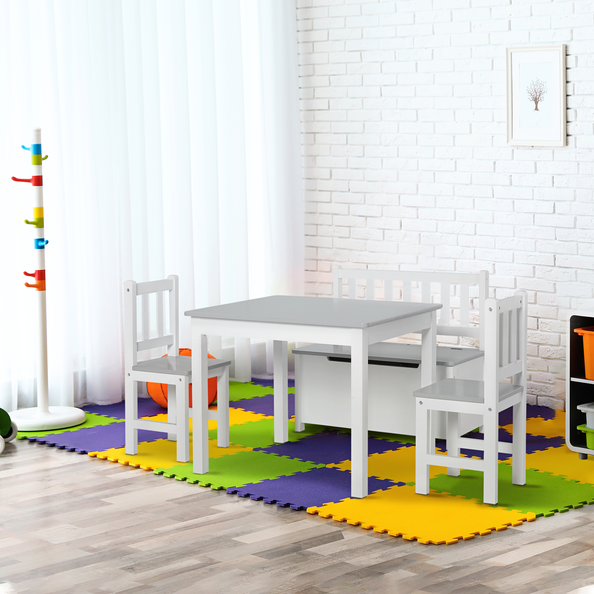 Un'area giochi per bambini con tavolo, sedie e panca contenitore. Tappetini colorati.