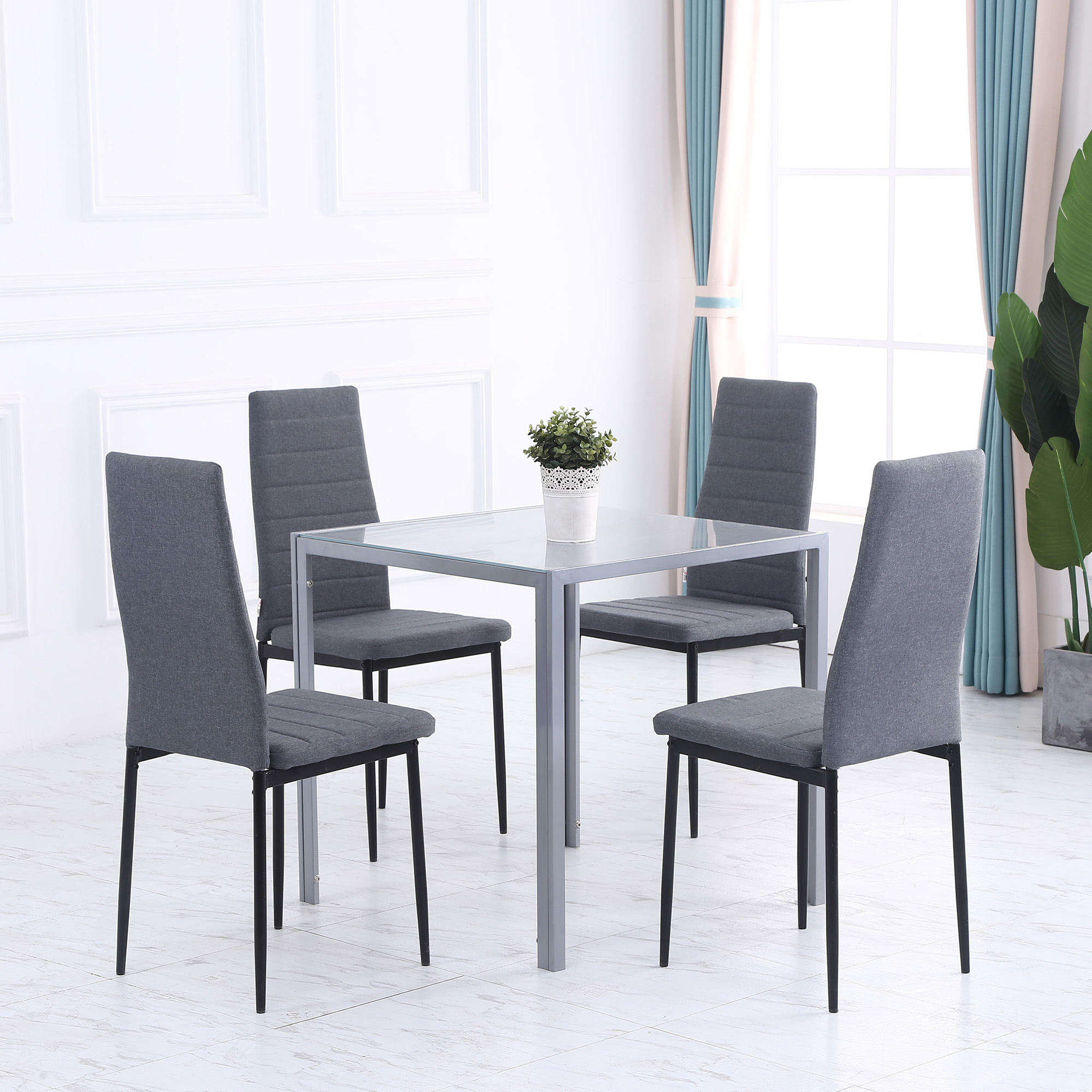 Set da pranzo con quattro sedie grigie attorno a un tavolo con piano in vetro.