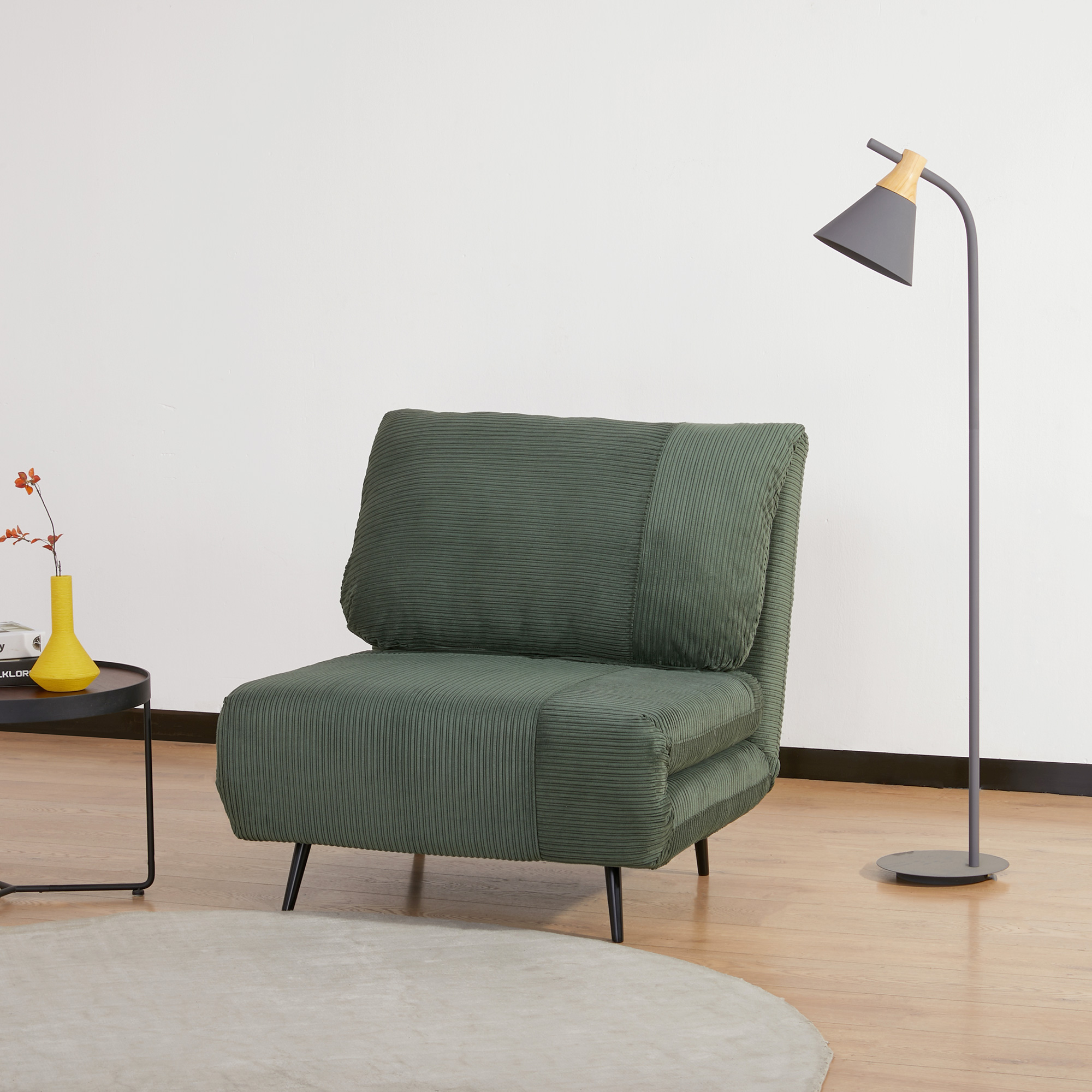 Sedia in velluto a coste verde. Tavolo nero con vaso giallo. Lampada da terra. Interno.