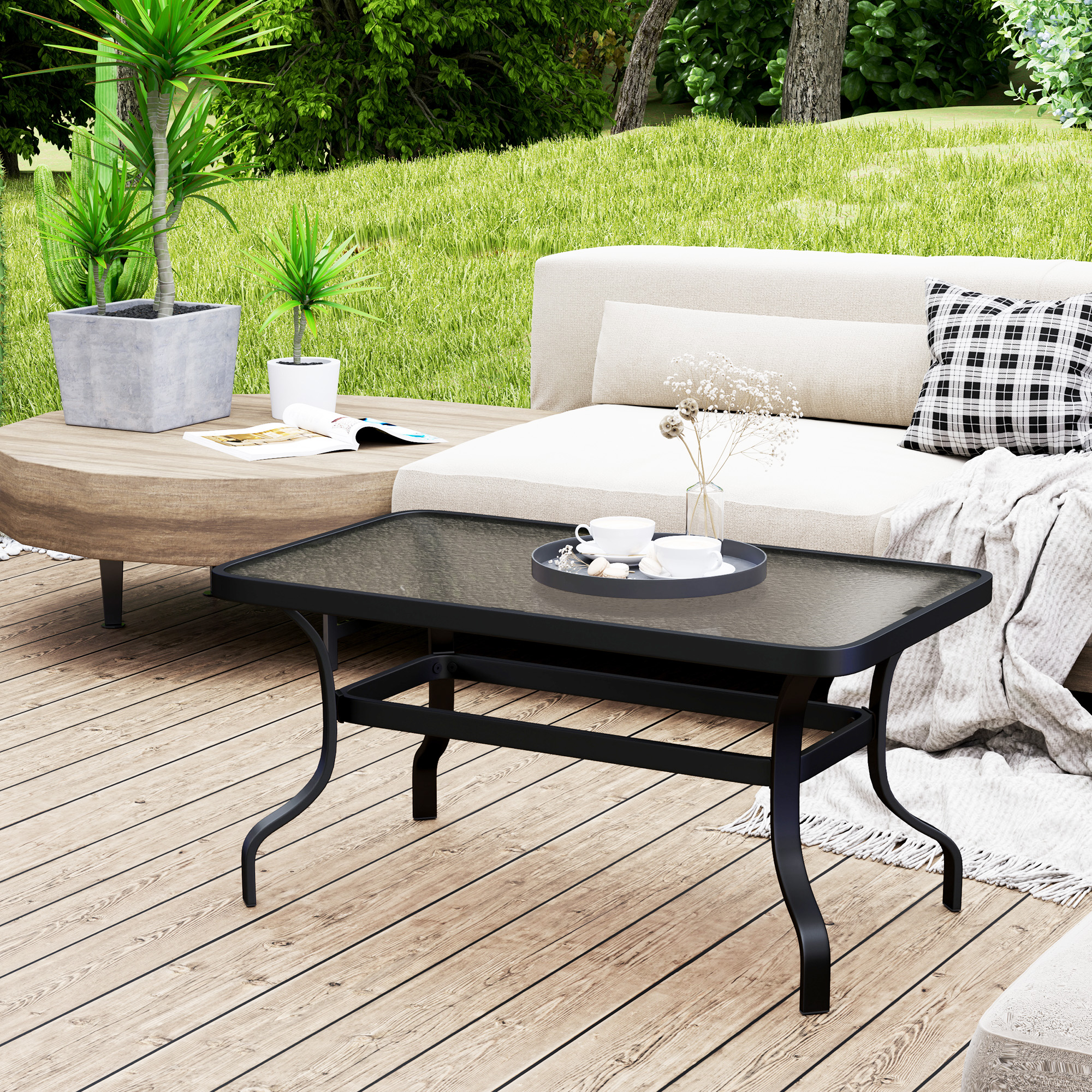 Un tavolino nero su un terrazzo in legno ha due tazze su un vassoio, un divano bianco e un prato verde.