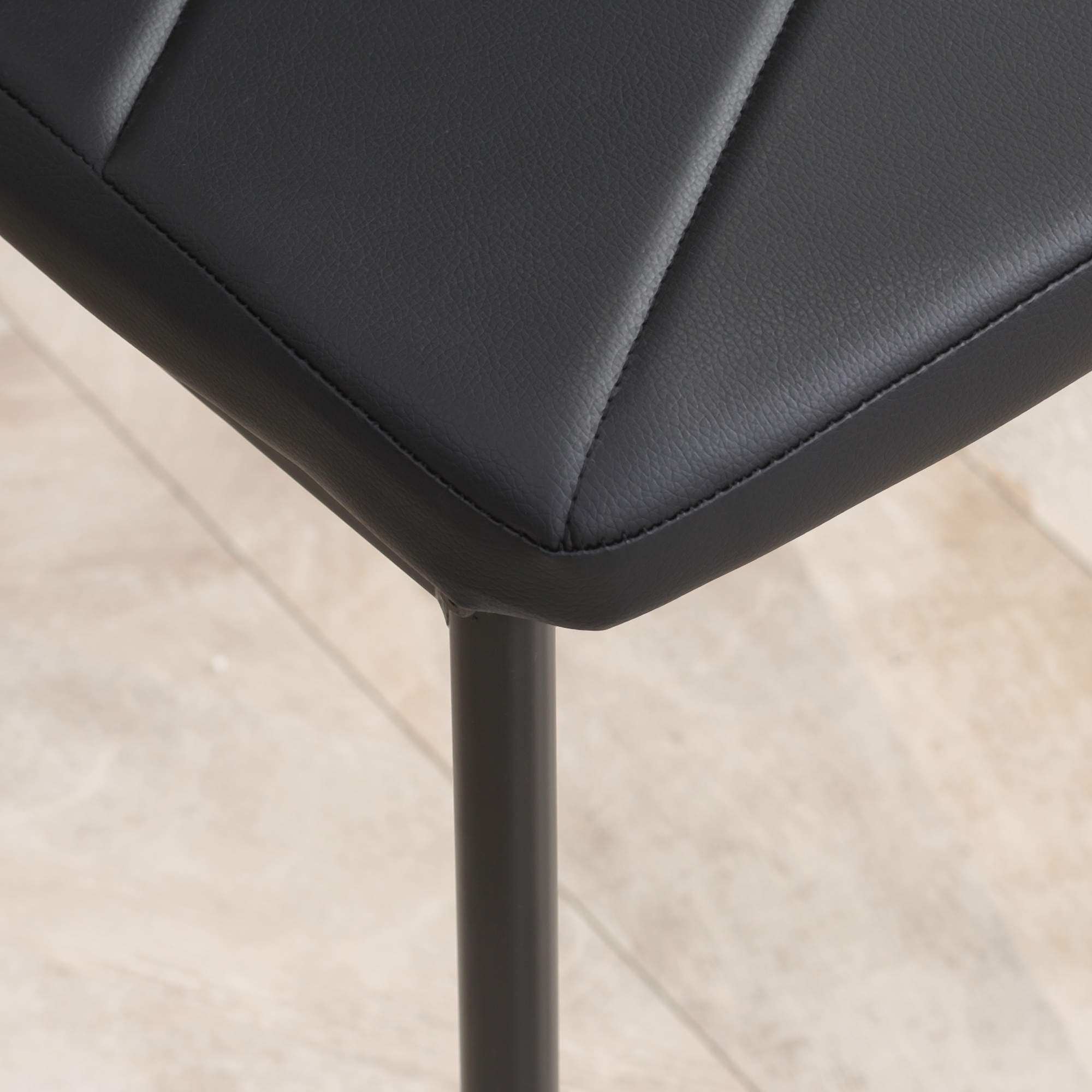 Sedile di sedia in pelle nera con cuciture su pavimento in legno chiaro.