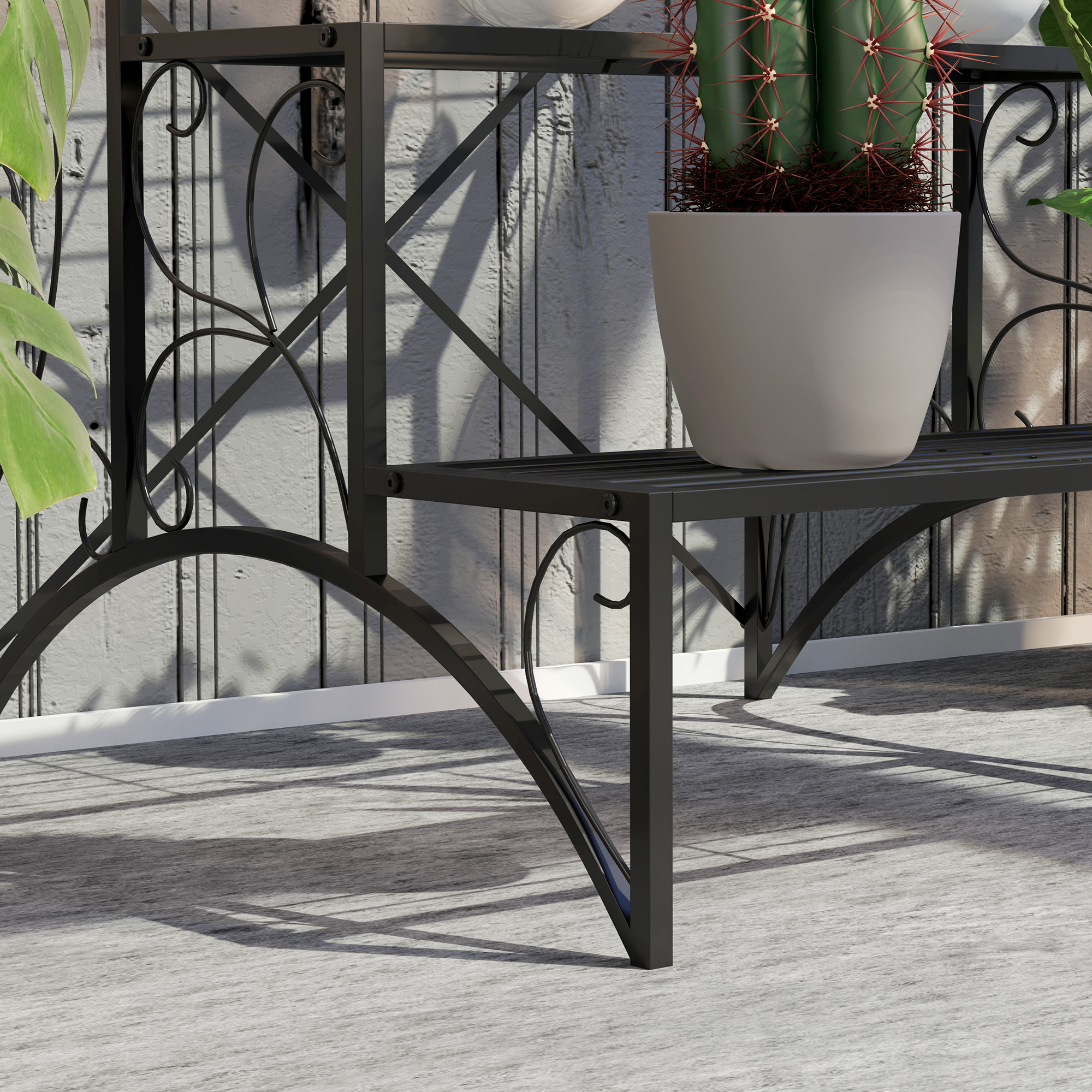 Primo piano di un supporto per piante in metallo nero con un cactus in un vaso bianco. Sfondo muro grigio.