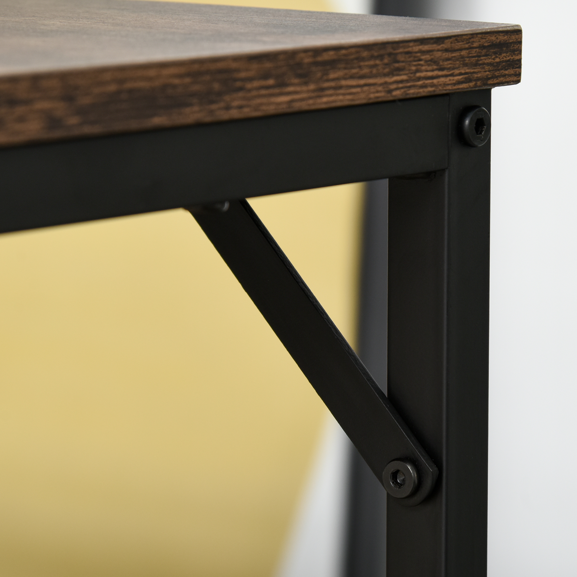 Angolo di scrivania in legno con telaio in metallo nero e viti. Parete gialla e bianca.