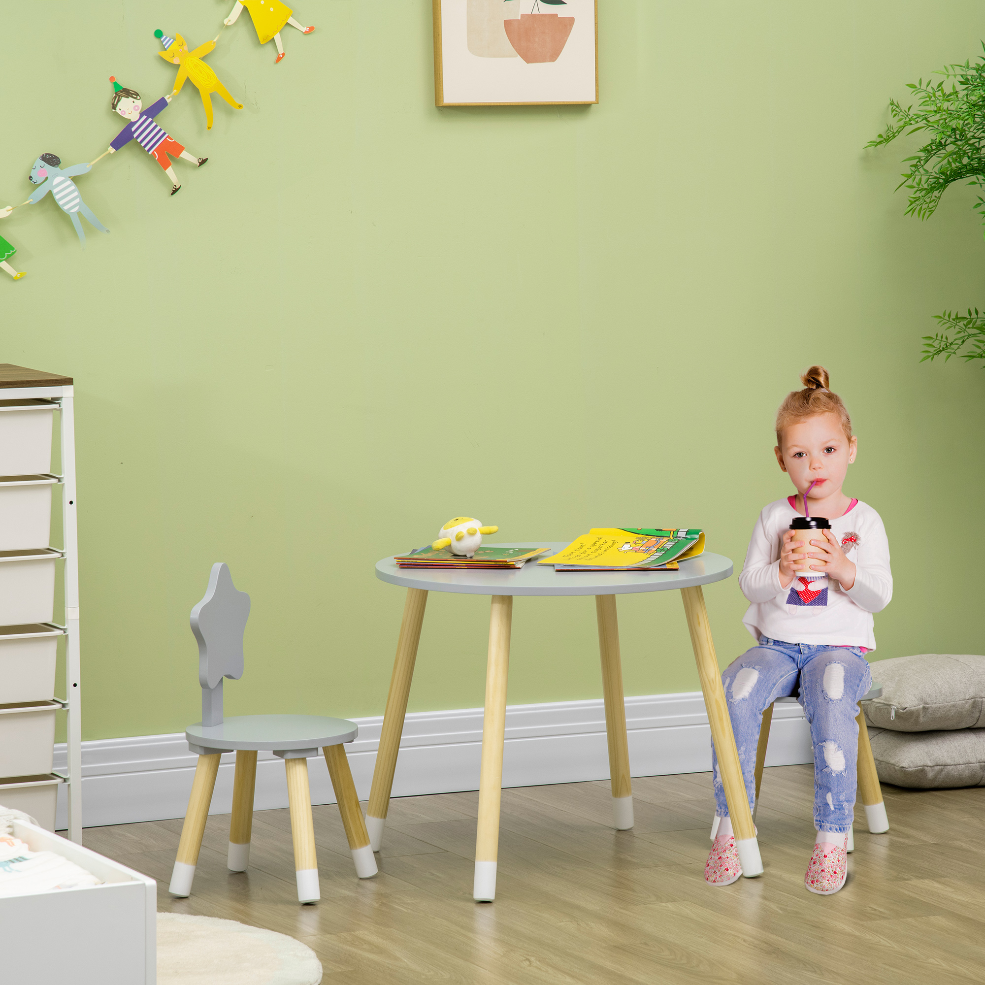 Una bambina a un tavolino con libro e bevanda, sedia a stella. Parete verde con decorazioni.