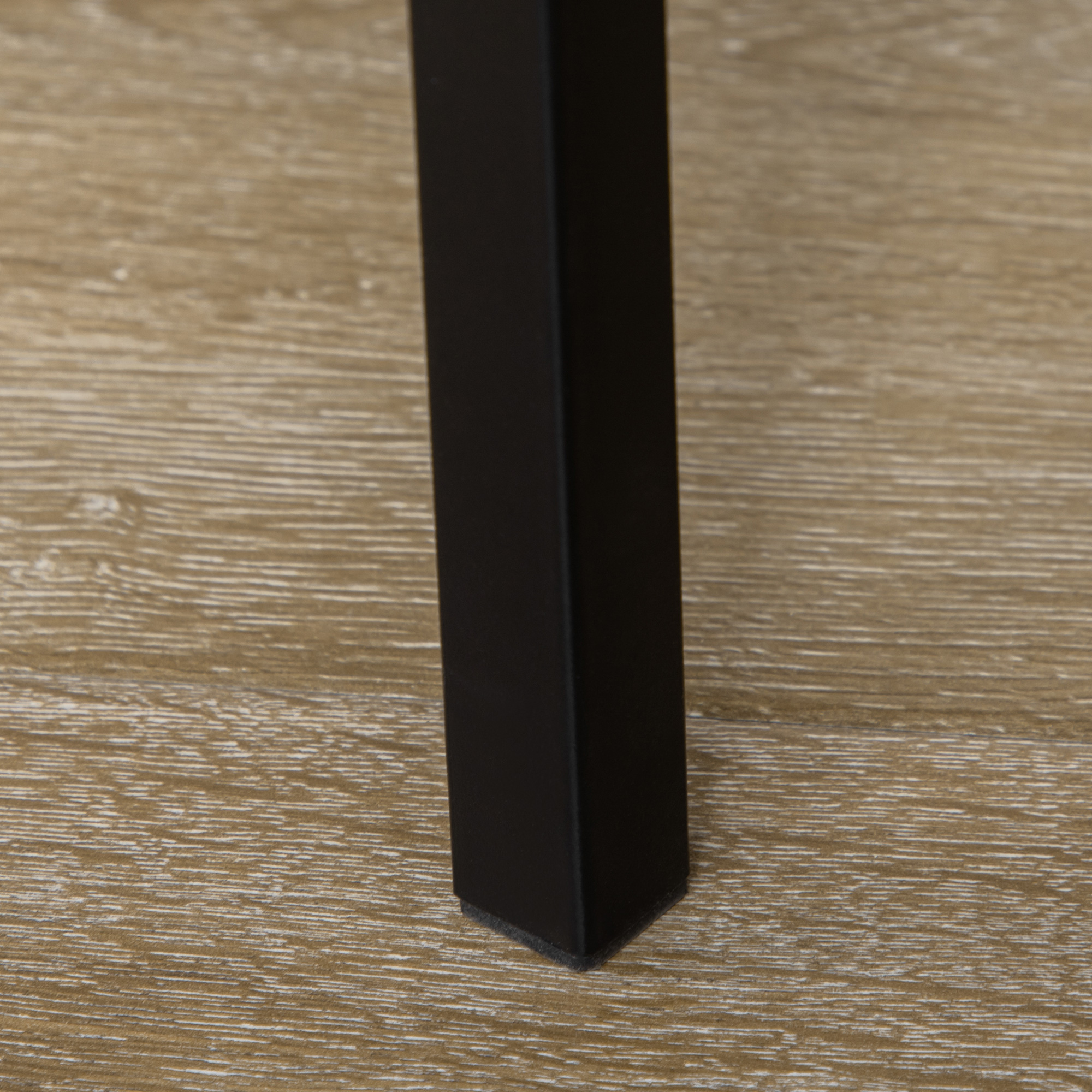 Gamba del tavolo nera su pavimento in legno. La gamba è di forma quadrata.