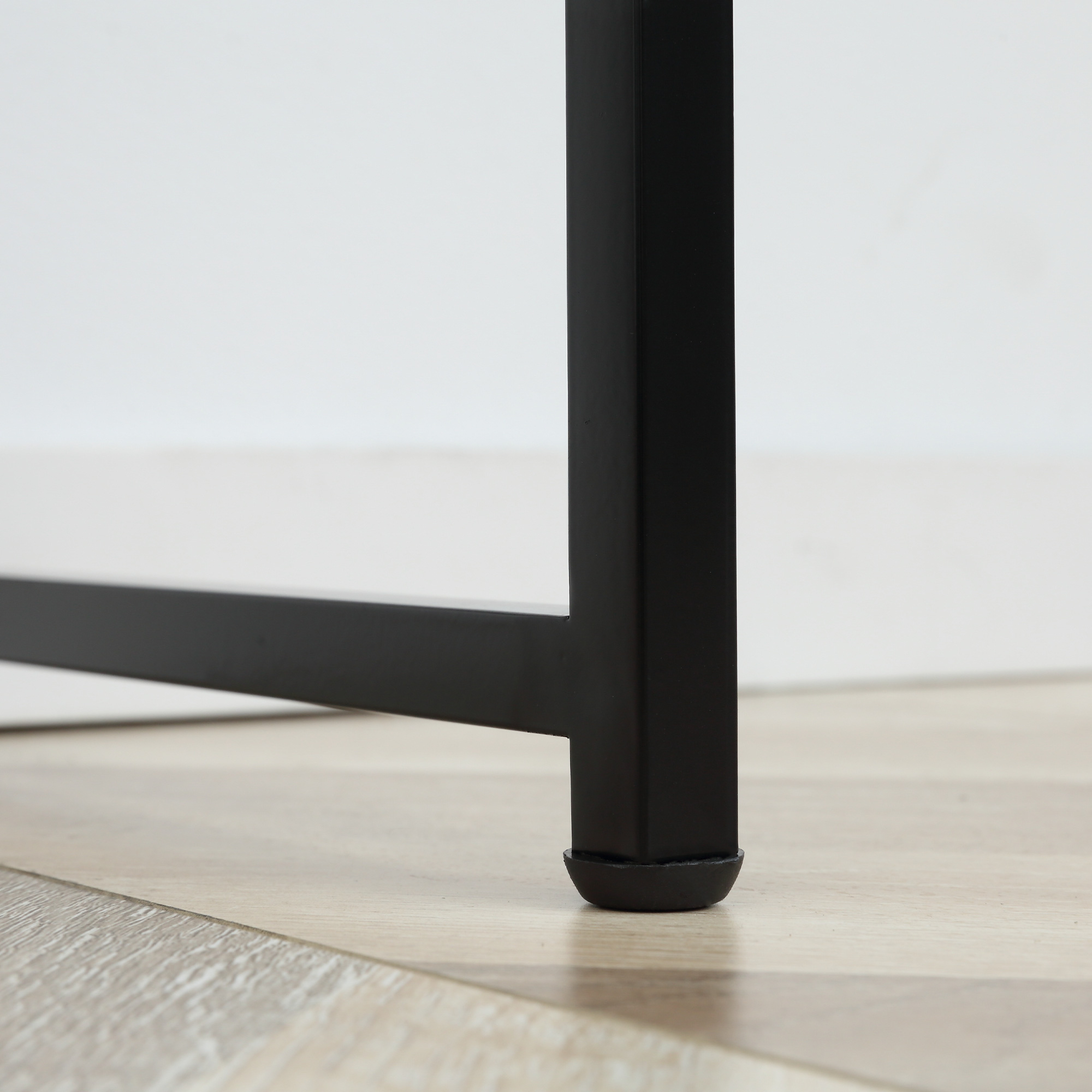 Primo piano di una gamba di tavolo nera su un pavimento in legno chiaro. La gamba ha un fondo in gomma.