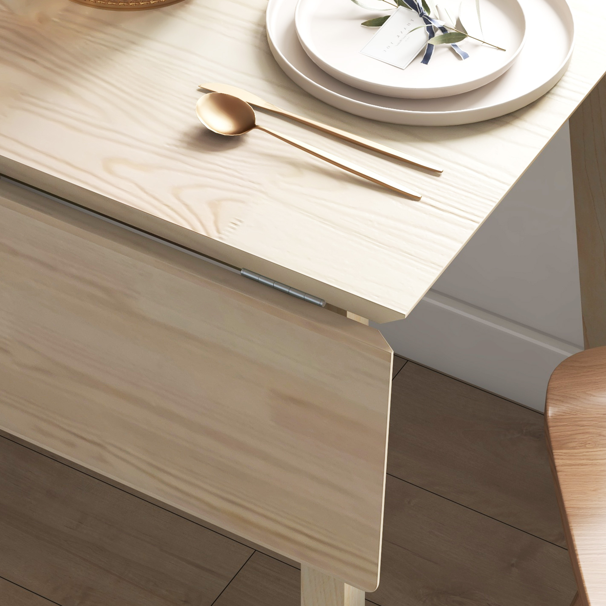 Ein Holztisch mit einem gefalteten Blatt, mit Tellern und Besteck darauf. Ein brauner Holzboden ist sichtbar.