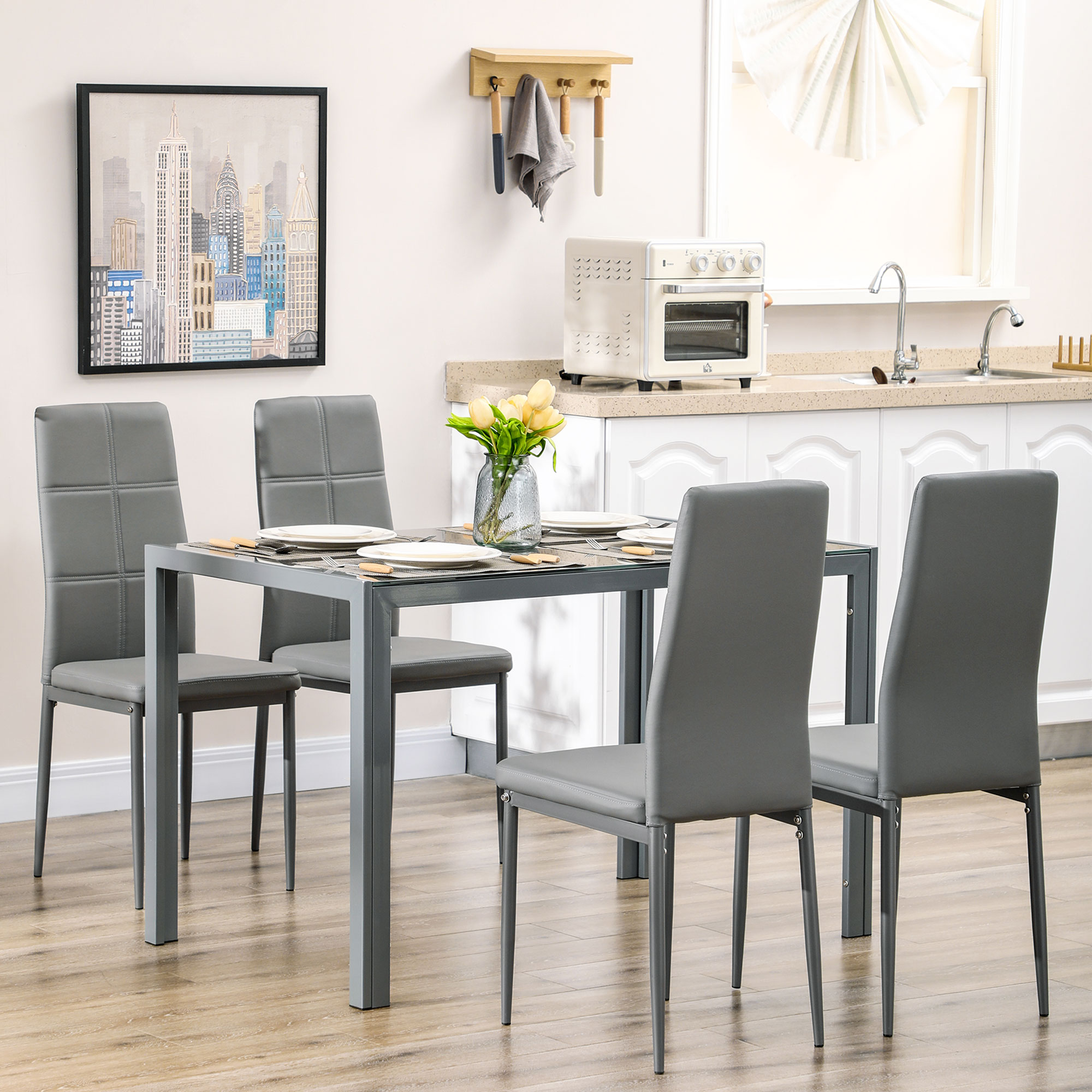 Set da pranzo con tavolo in vetro, quattro sedie grigie e sfondo cucina.