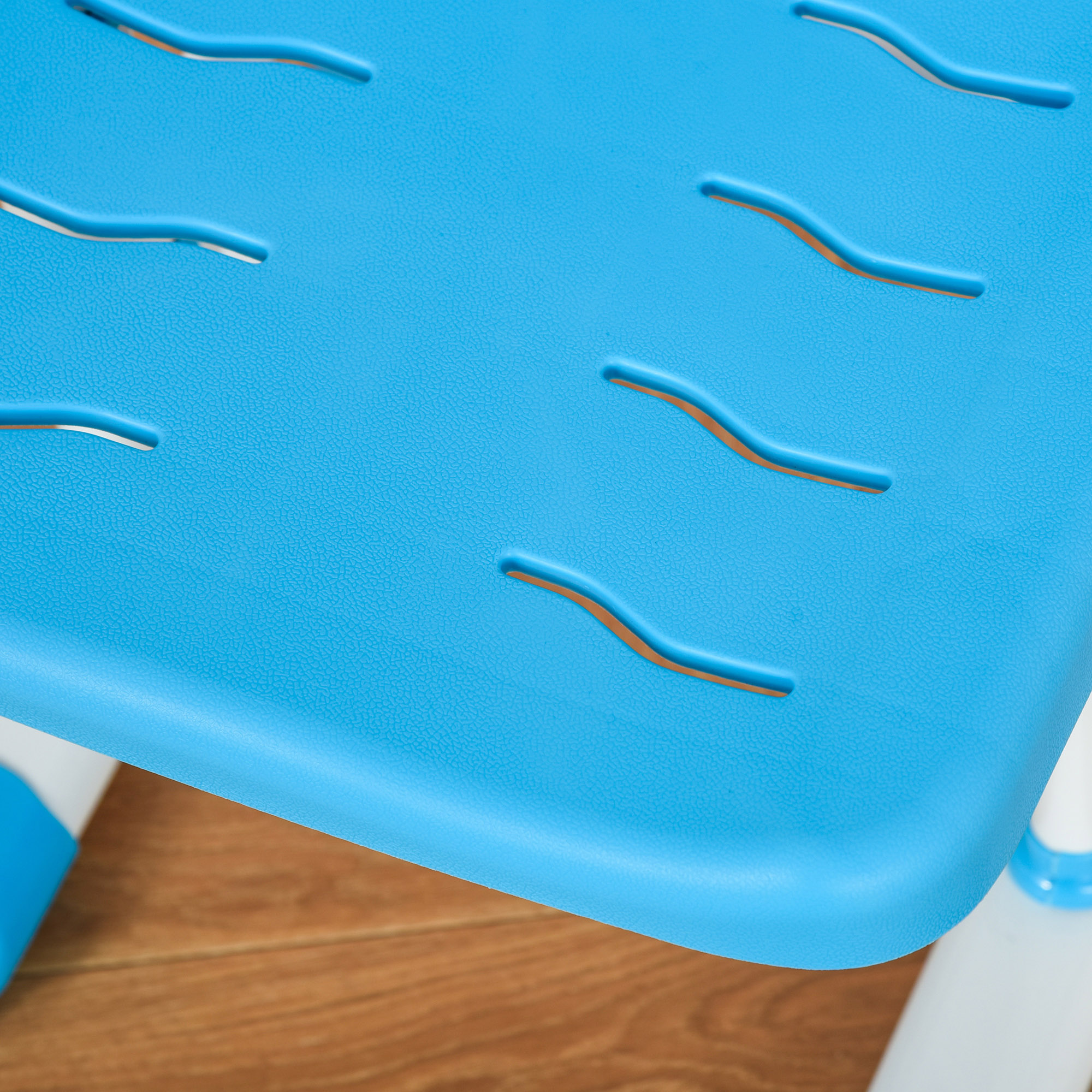 Primo piano di una seduta di sedia in plastica blu con disegni ritagliati, su pavimento in legno.