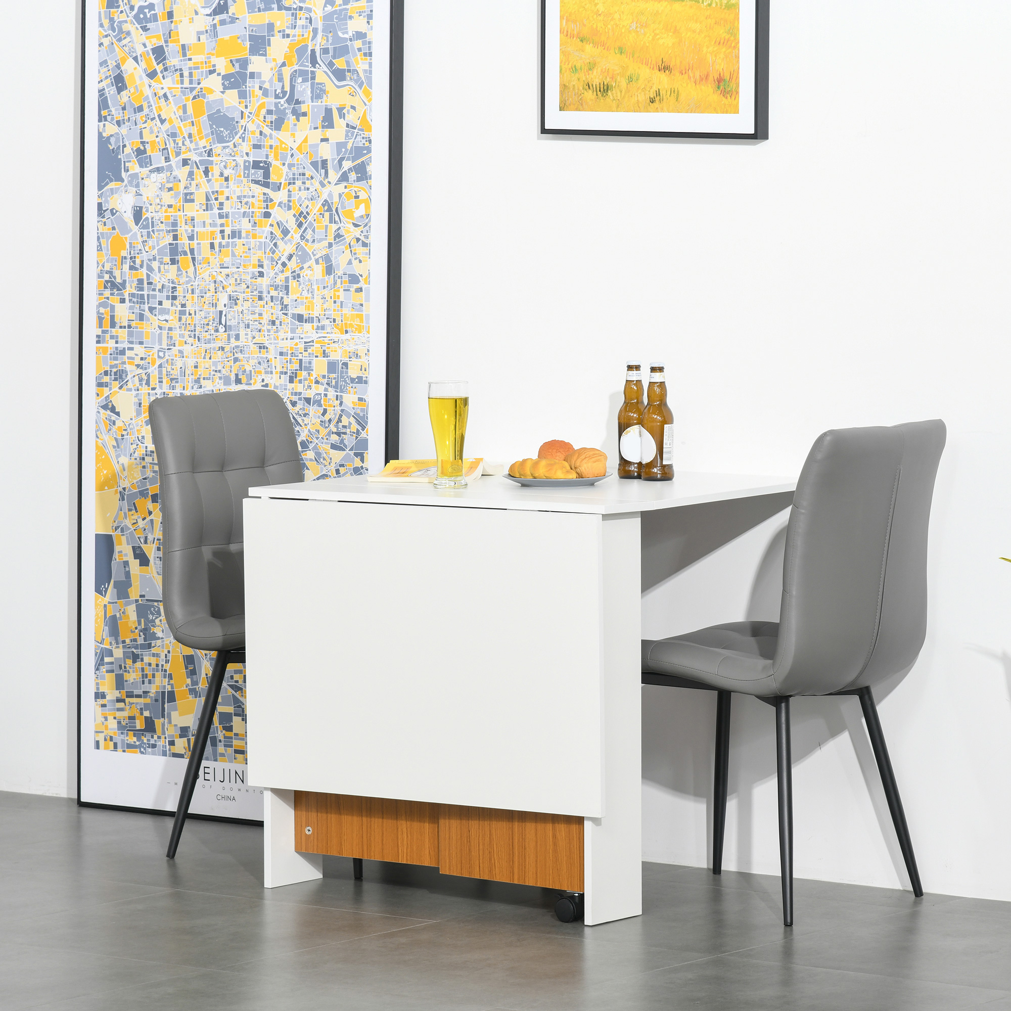 Mesa blanca pequeña con dos sillas grises. Un mapa de la ciudad y una pintura cuelgan en la pared. Cerveza y aperitivos.