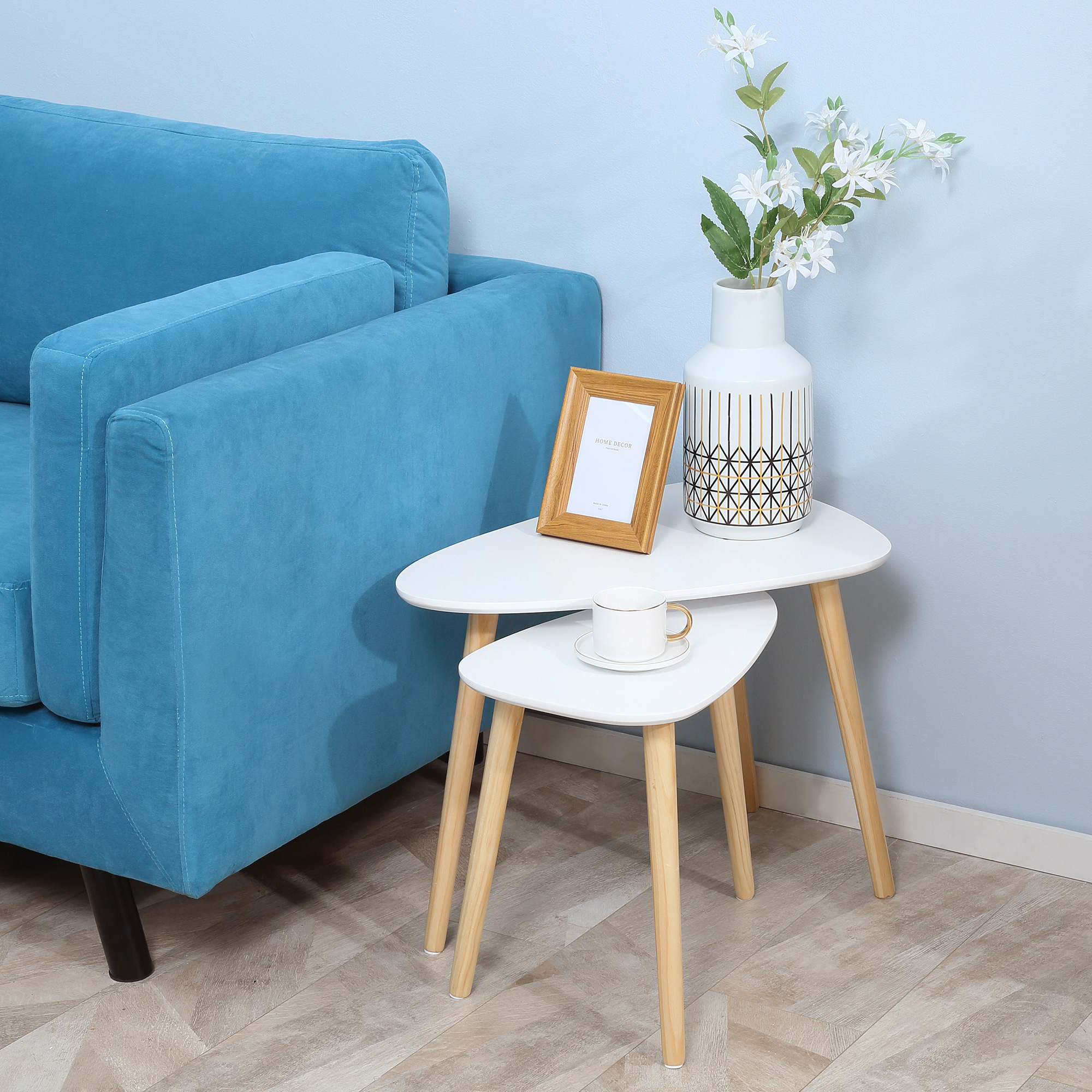 Tavolini bianchi ad incastro con vaso, cornice e tazza su muro blu.