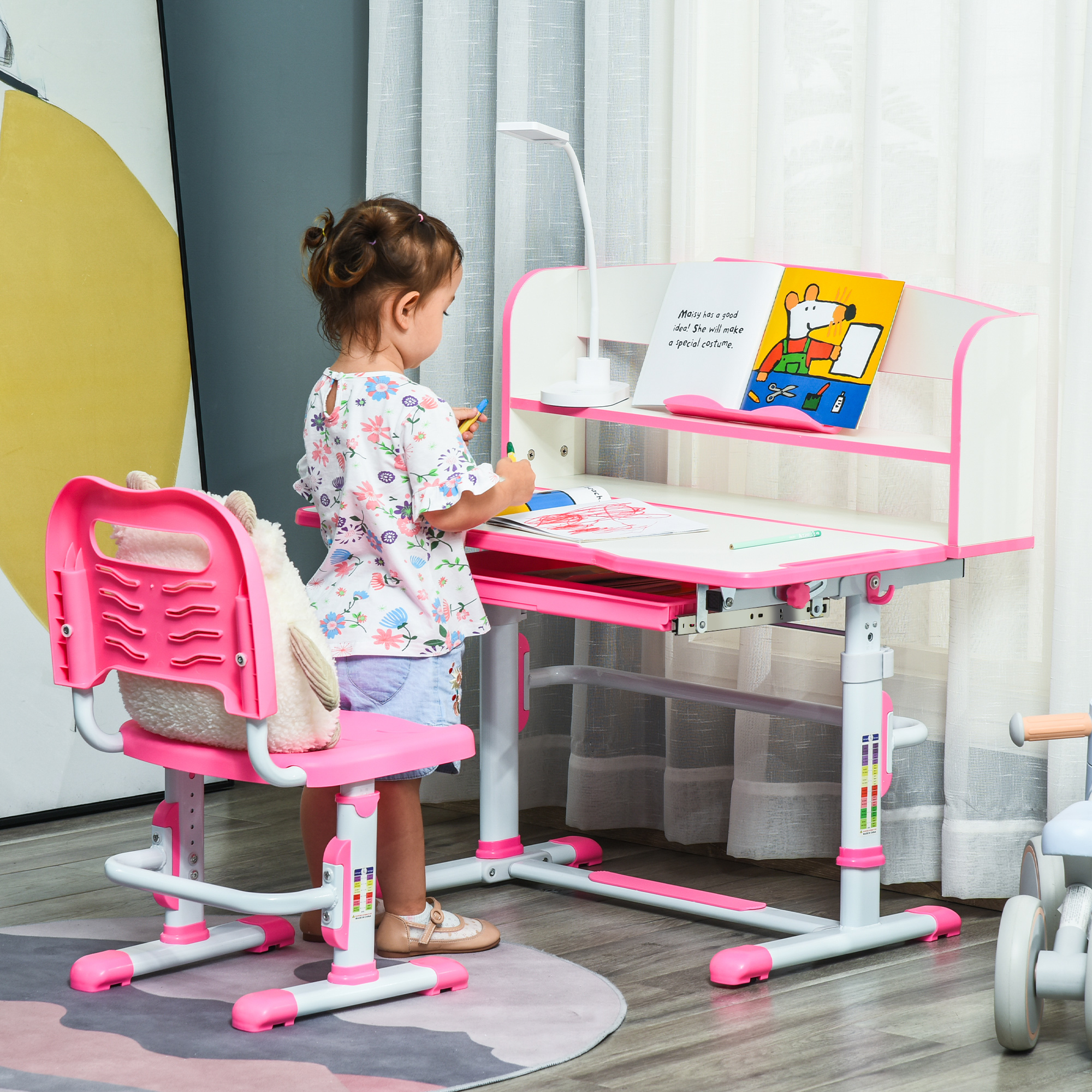 Un bambino è a una scrivania. La scrivania e la sedia sono rosa. Una lampada e un libro sono sulla scrivania.