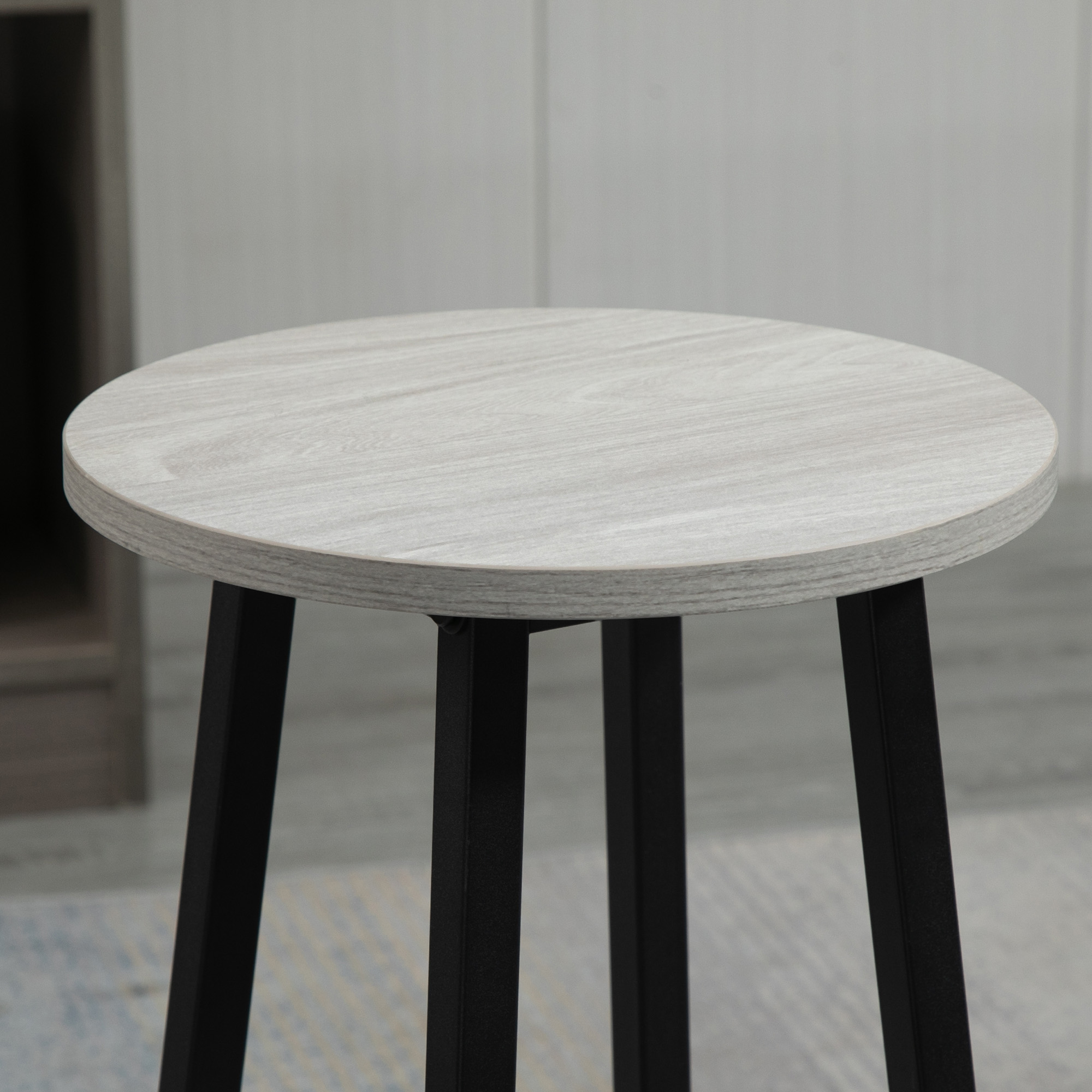 Uno sgabello in legno grigio chiaro con gambe nere. La parte superiore è rotonda.