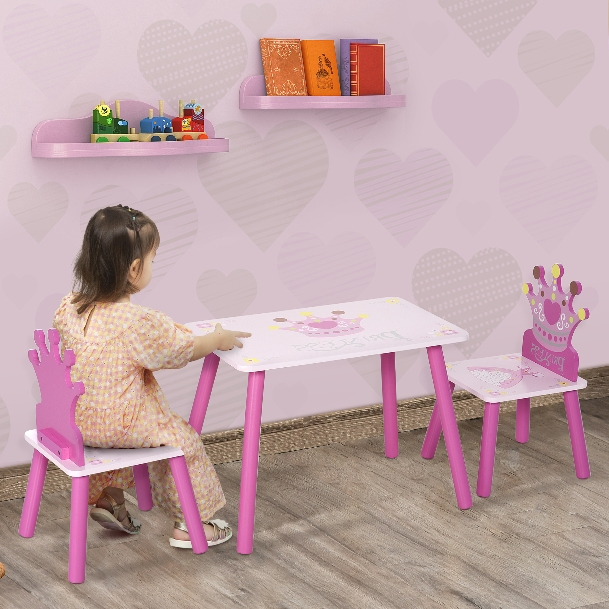 Un bambino piccolo è seduto a un tavolo rosa con due sedie abbinate. Libri e giocattoli sugli scaffali.