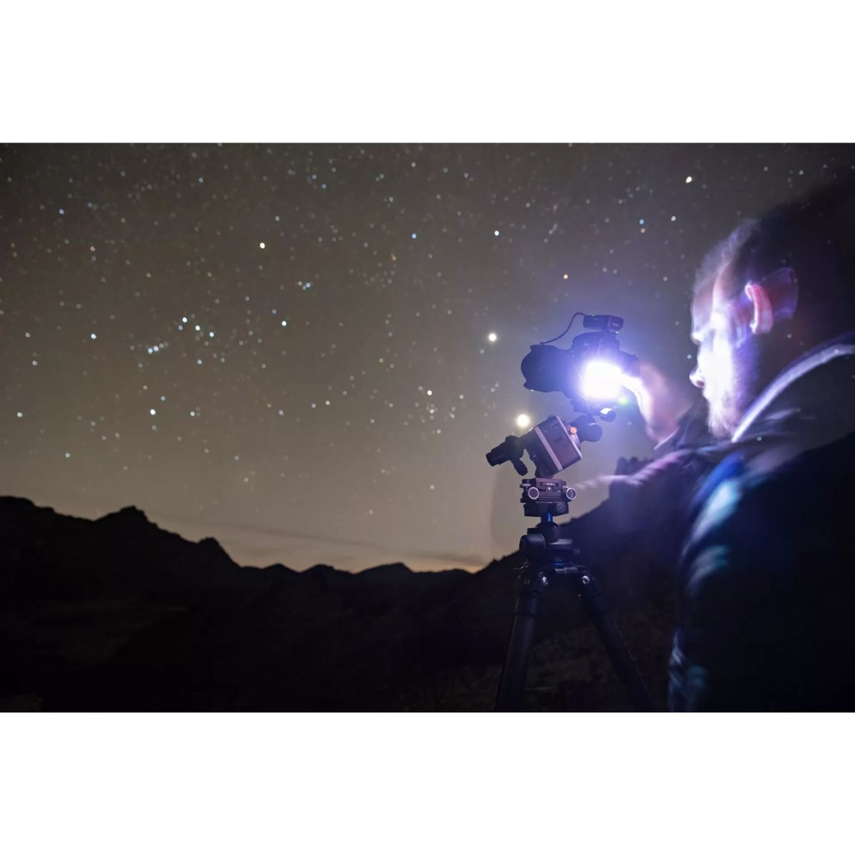 Persona con telescopio observando el cielo nocturno con estrellas.