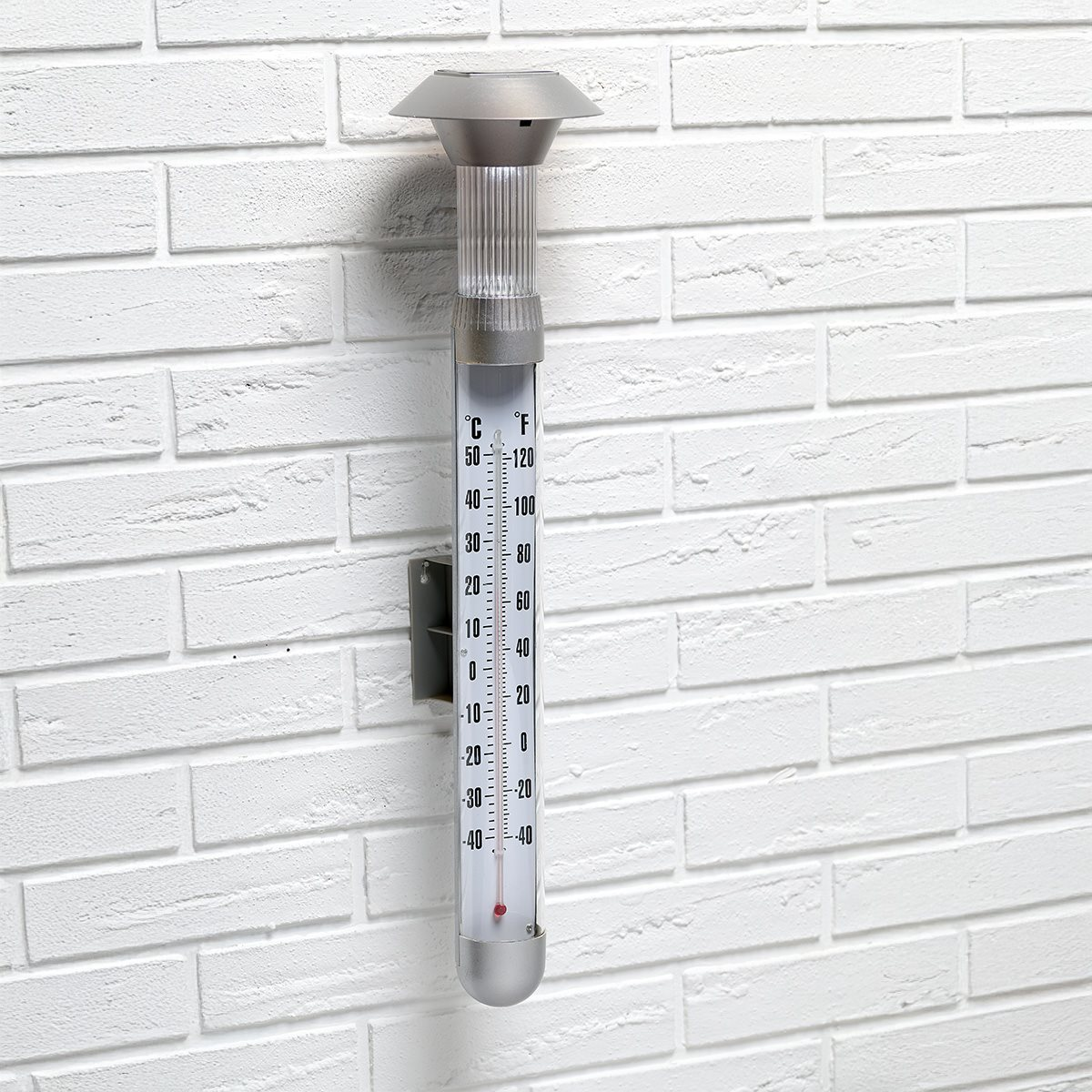 A solar-powered thermometer is mounted on a white brick wall. It shows the temperature.