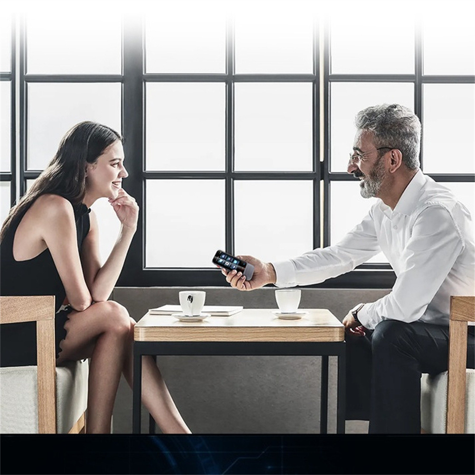 Zwei Personen sitzen und unterhalten sich an einem Tisch. Eine Person hält ein Telefon, die andere lächelt.