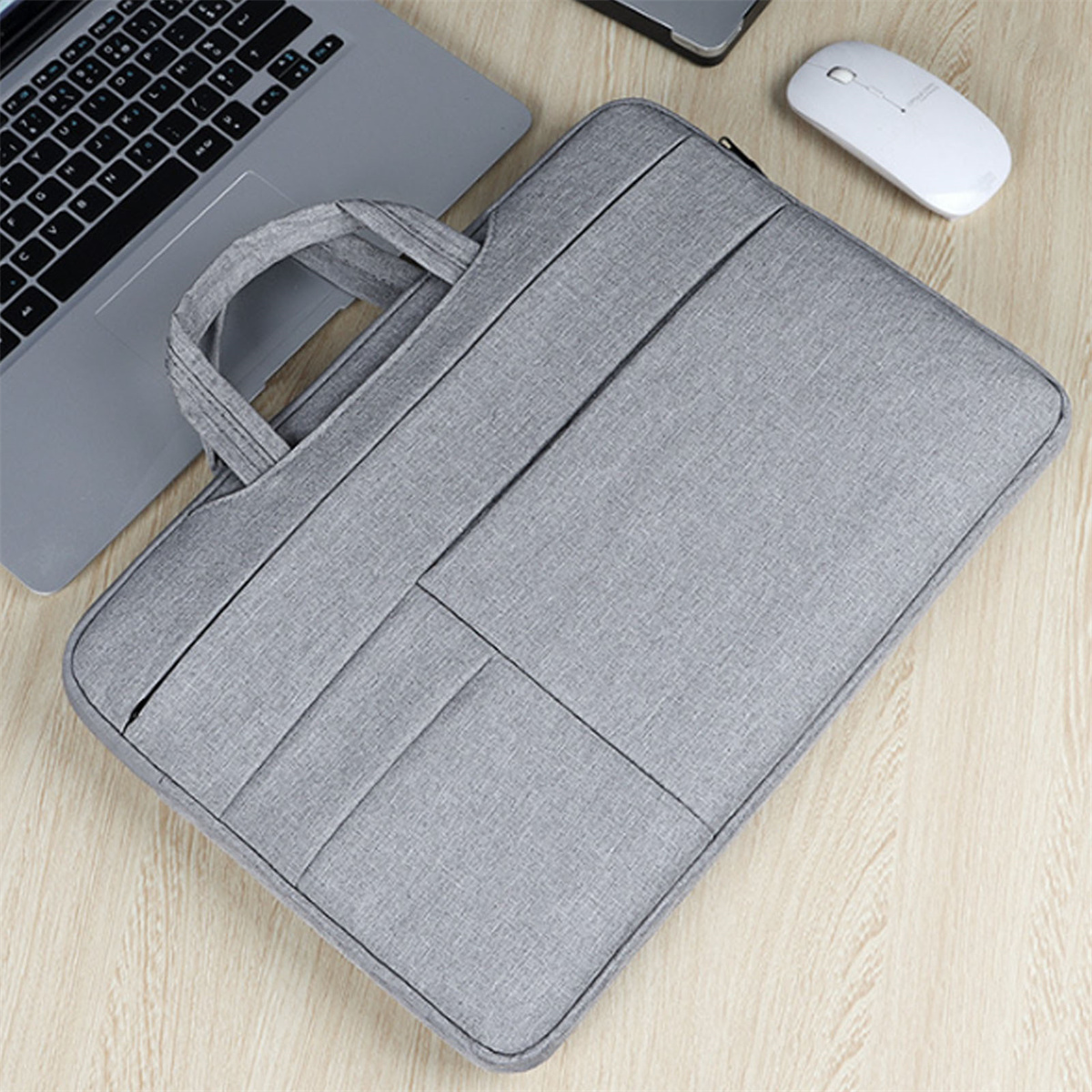 Eine graue Laptoptasche auf einem Holztisch mit Laptop, Maus und Ladekabel. Die Tasche hat einen Griff.