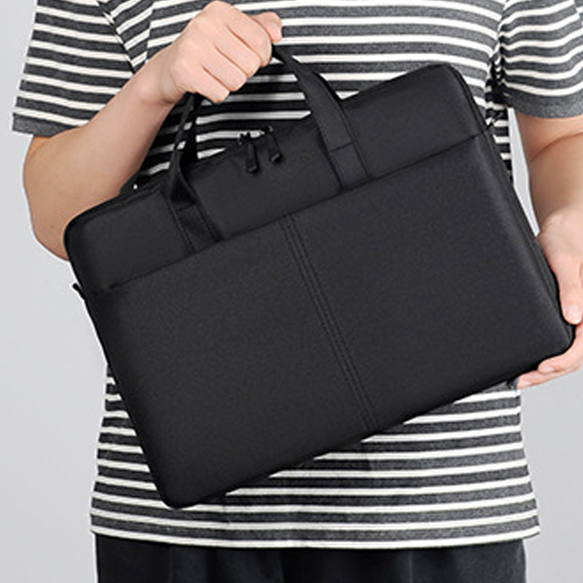 Eine Person hält eine schwarze Laptop-Tasche. Die Tasche ist rechteckig, mit Griffen und einem Reißverschluss.