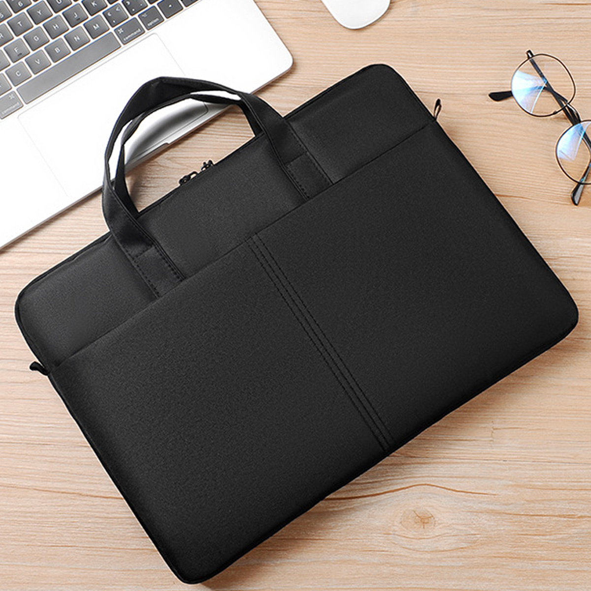 Schwarze Laptoptasche auf einem Holzschreibtisch, mit Laptop, Brille und Maus.