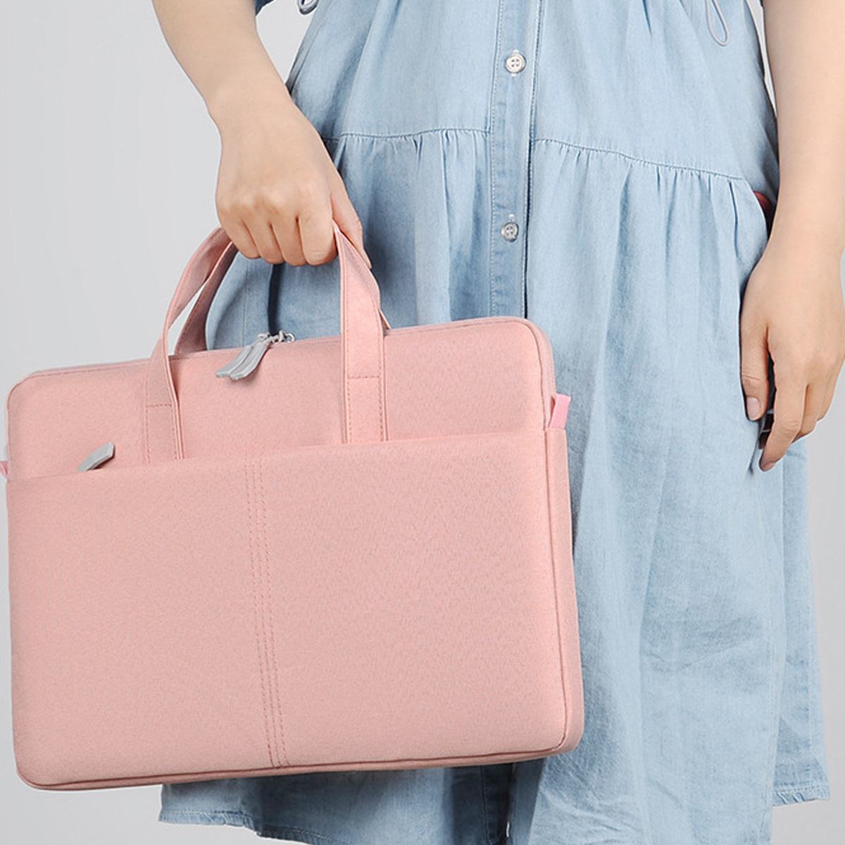 Eine Person, die eine rosa Laptoptasche hält, trägt ein blaues Kleid, neutraler Hintergrund.