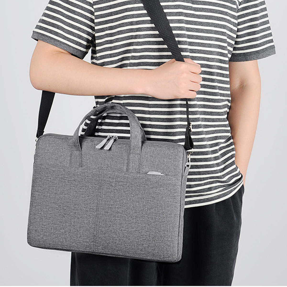 Ein Mann mit einer grauen Laptoptasche über der Schulter, steht und hält den Griff der Tasche.