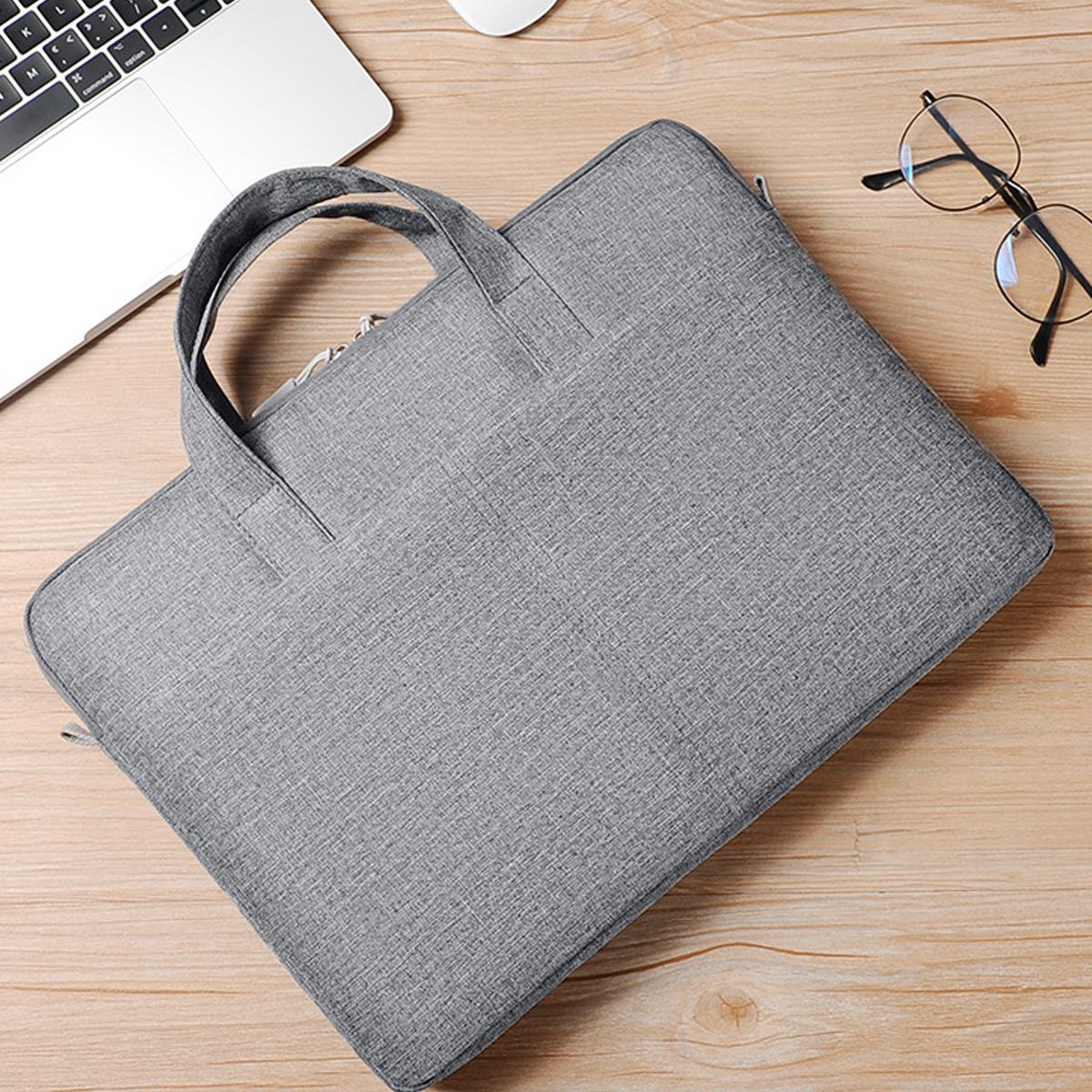 Graue Laptoptasche auf einer Holzoberfläche. Ein Laptop und eine Brille sind in der Nähe sichtbar.