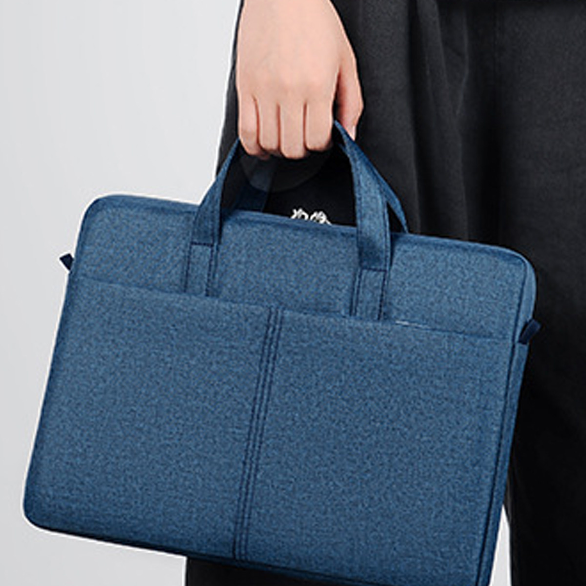 Eine Person hält eine blaue Laptop-Tasche aus Stoff mit zwei Vordertaschen und einem Griff.