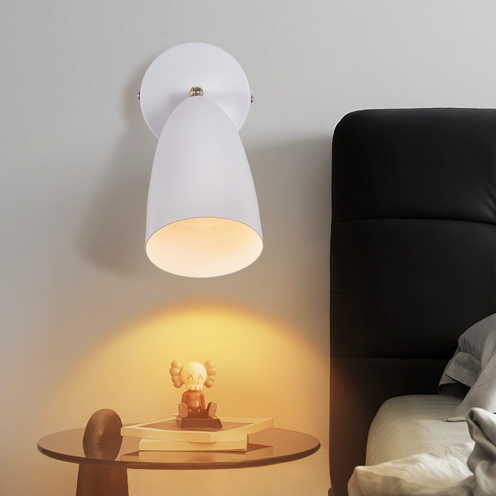 Una lampada bianca a parete con una testa direzionale, che proietta la luce su un tavolo con una figura.