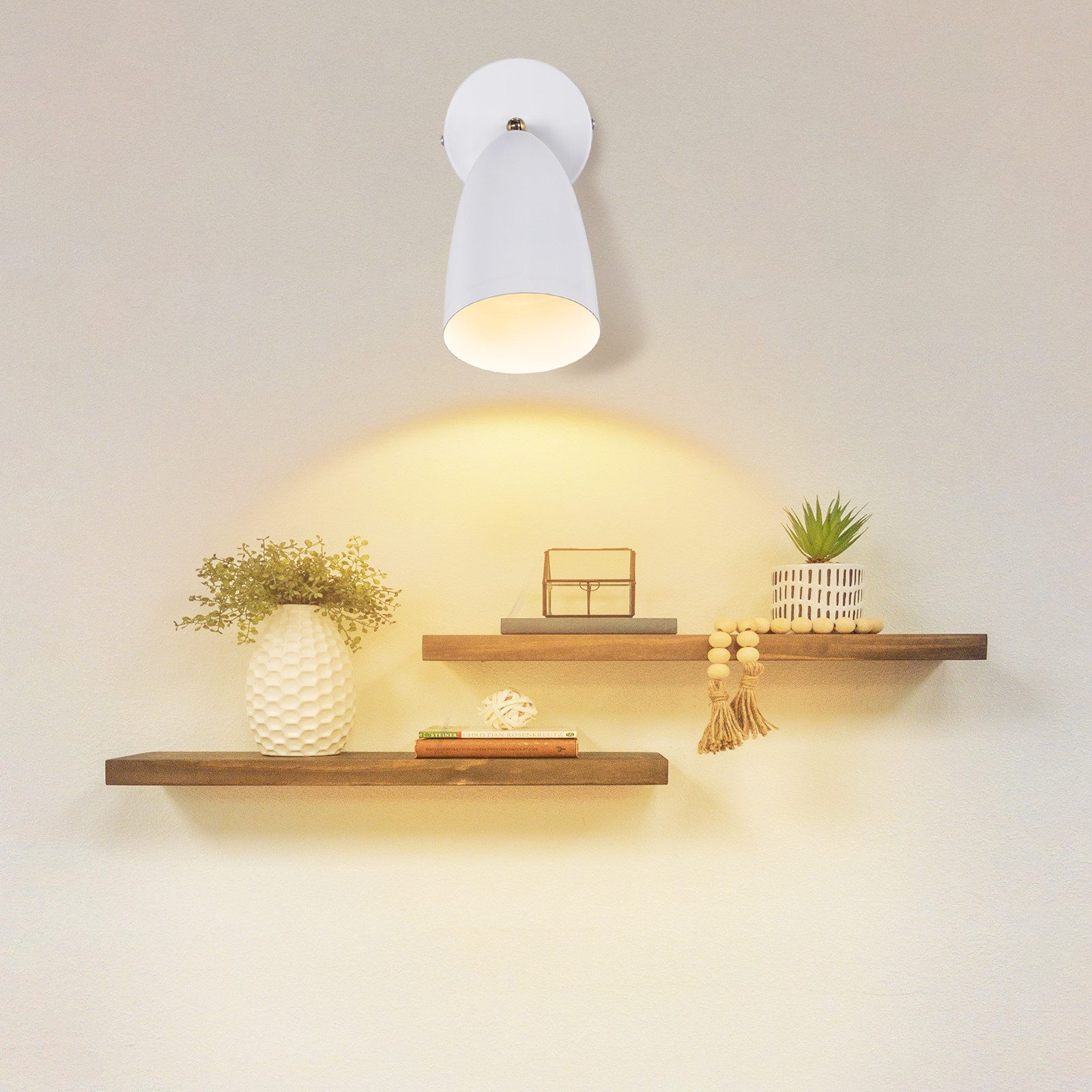 Lampada bianca a parete con luce direzionale. Sotto ci sono mensole e decorazioni.