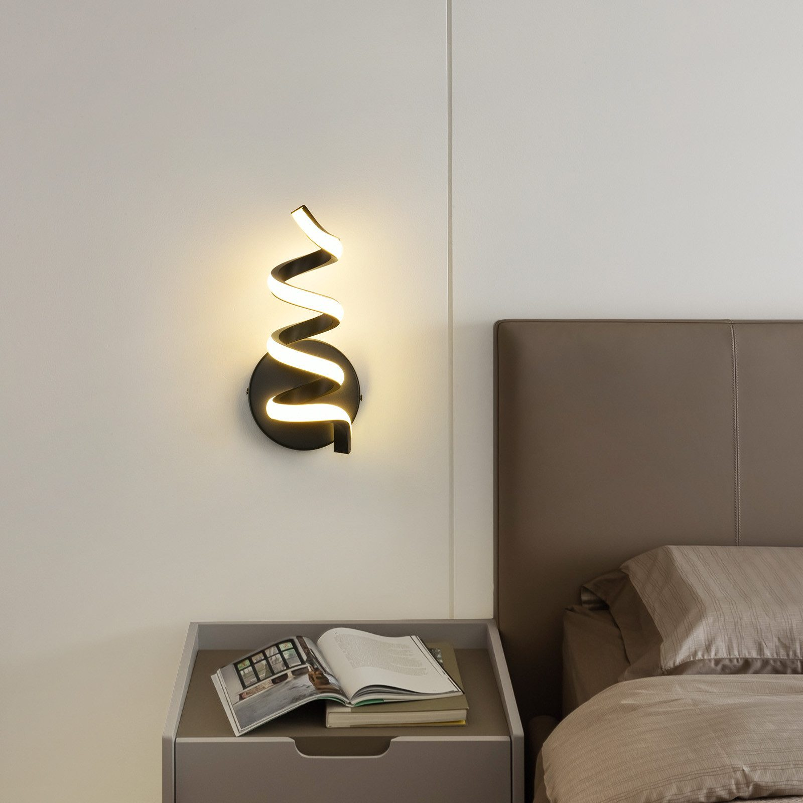 Lampada da parete a spirale moderna su un muro bianco accanto a un comodino con un libro. Il letto è a destra.