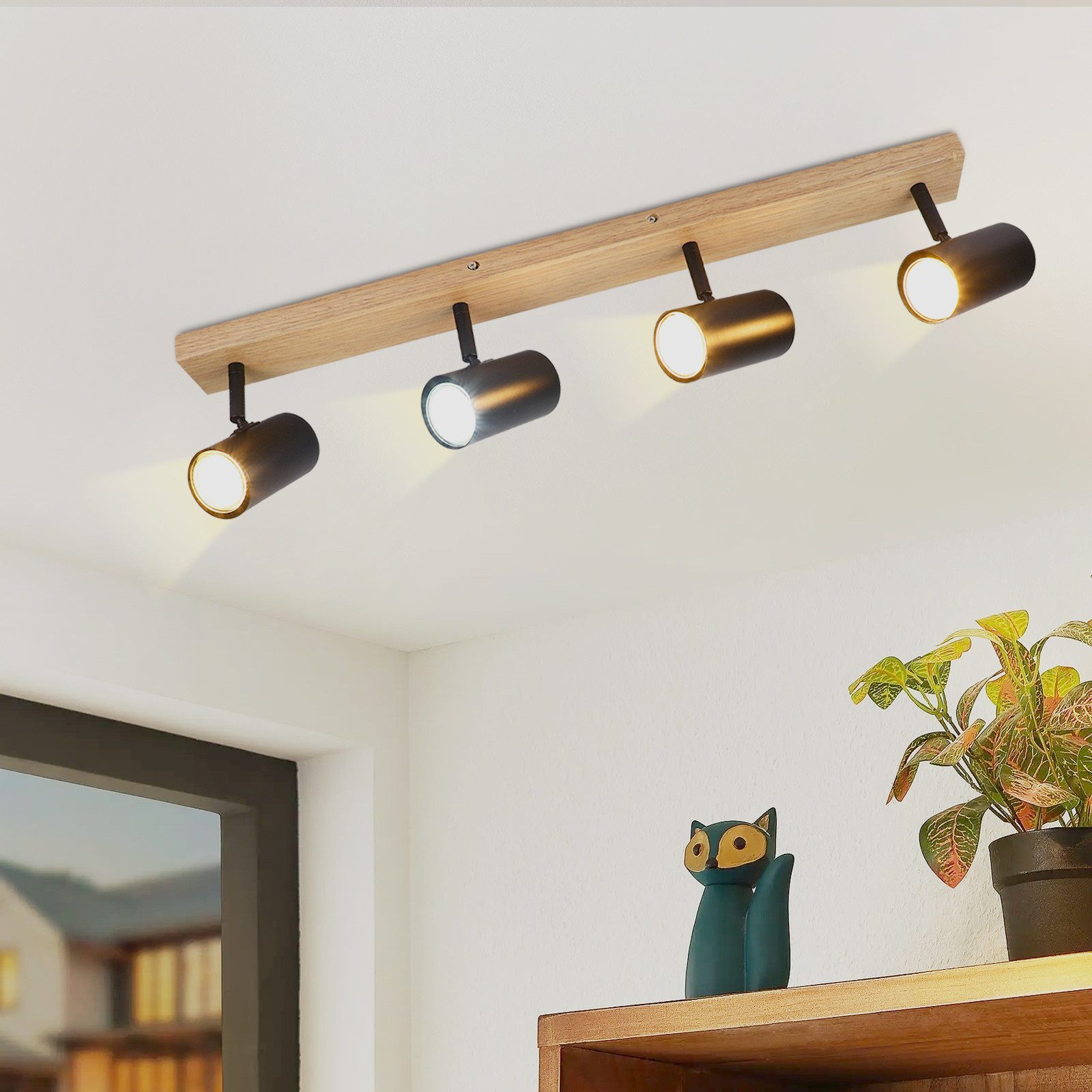 Faretti da soffitto moderni su una trave di legno, con una pianta e una statua di gatto sotto.