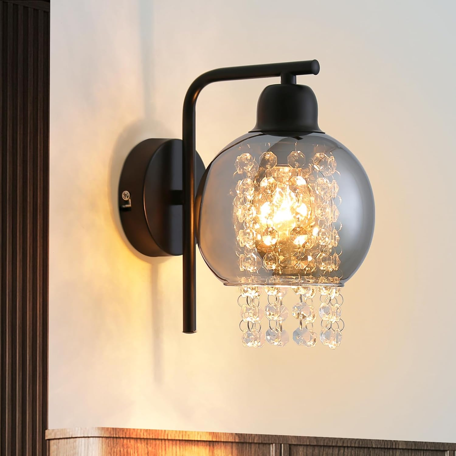Lampada da parete nera con paralume rotondo e pendente di cristallo. La luce è accesa.