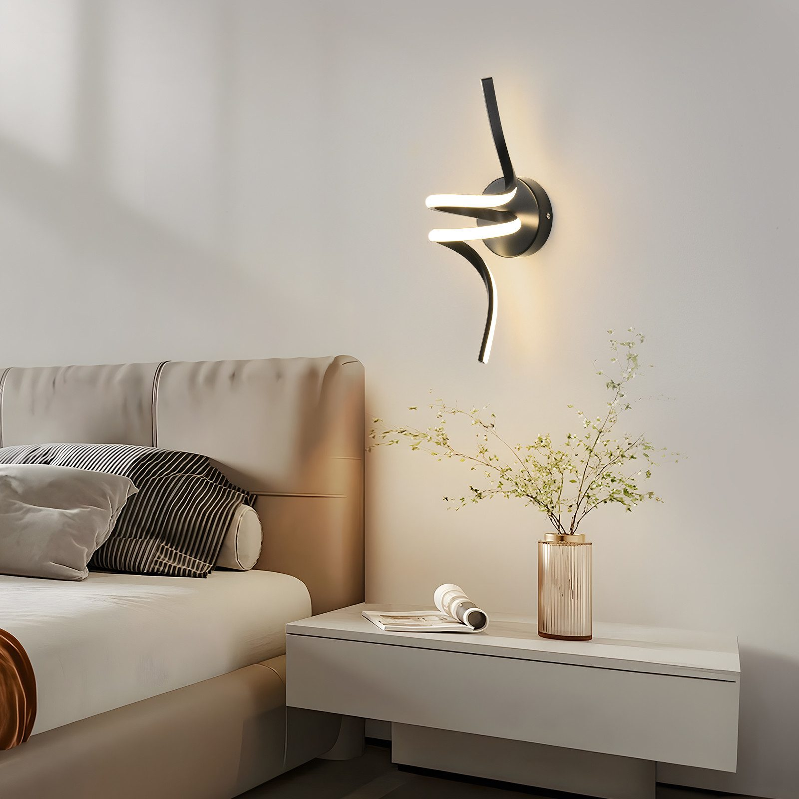 Una moderna lámpara de pared en un dormitorio. Tiene un acabado negro y un diseño abstracto. Un jarrón con flores está al lado.