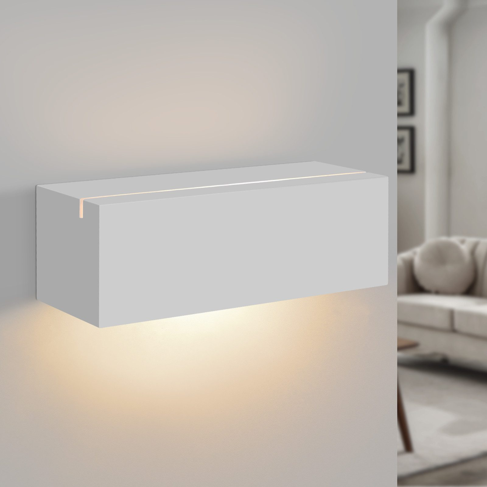 Una lampada da parete rettangolare bianca emette luce verso il basso, montata su un muro bianco. Include un divano.