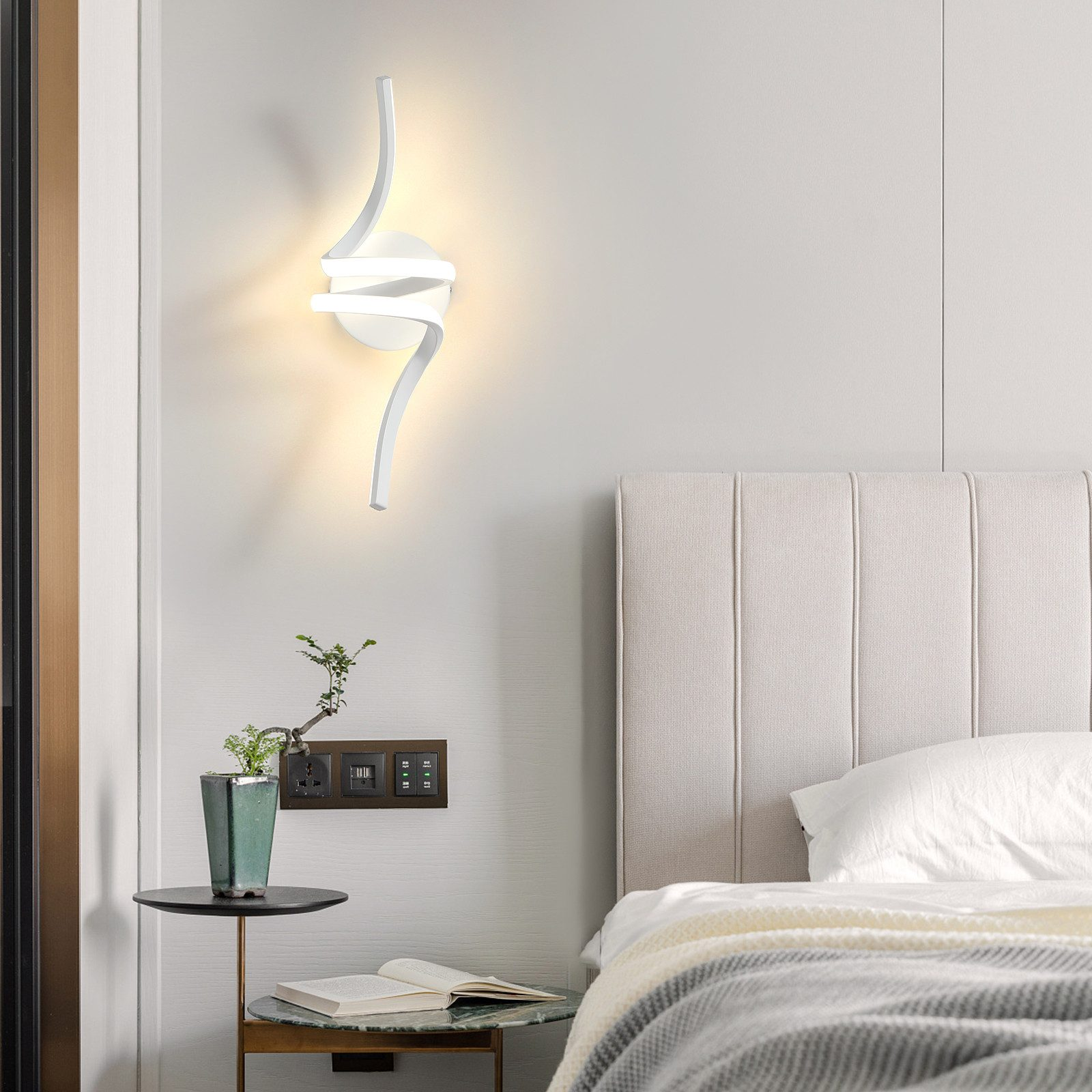 Lampada da parete bianca moderna con design astratto, sopra un letto.