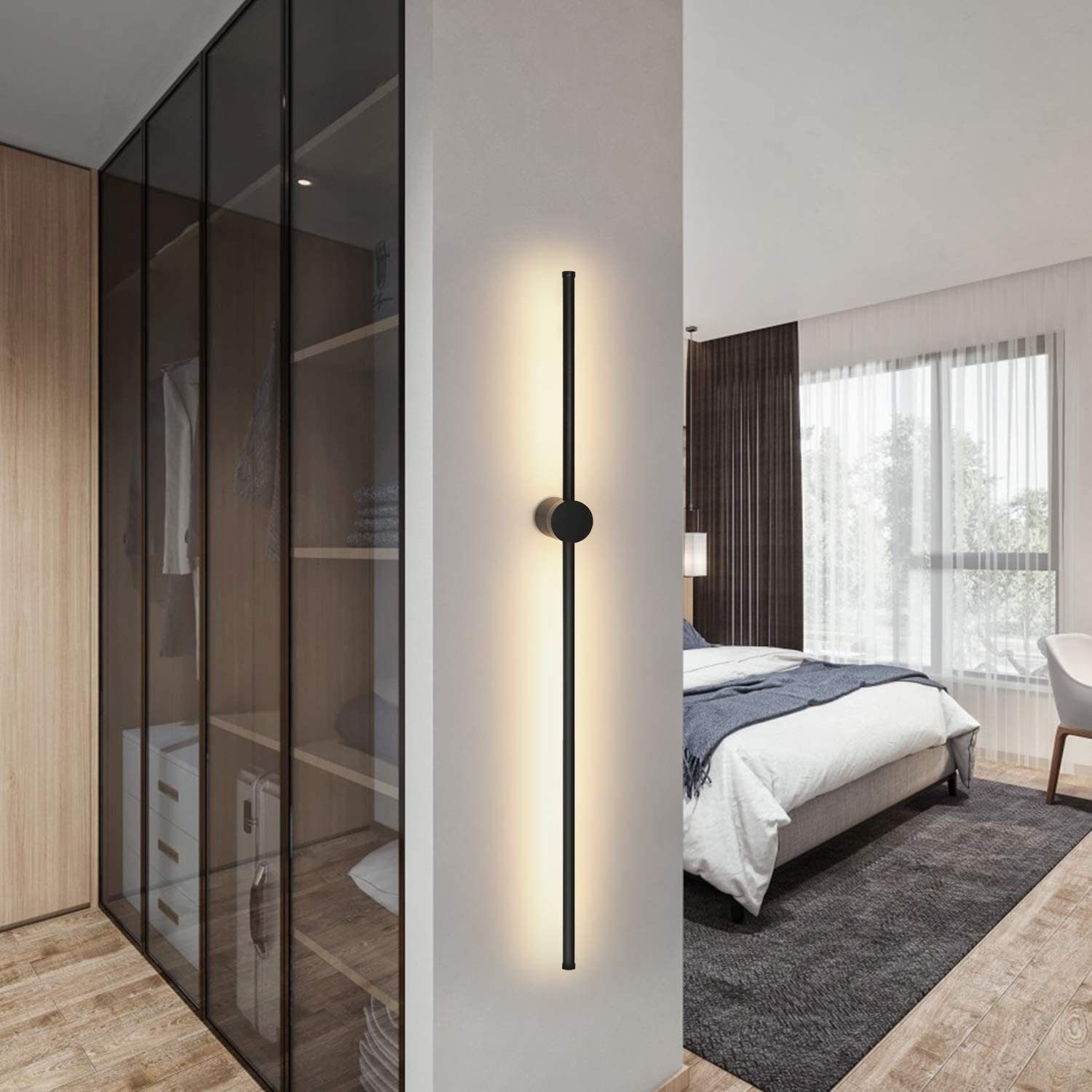 Lunga lampada da parete nera con luce bianca in una camera da letto. Armadio con ante in vetro a sinistra.