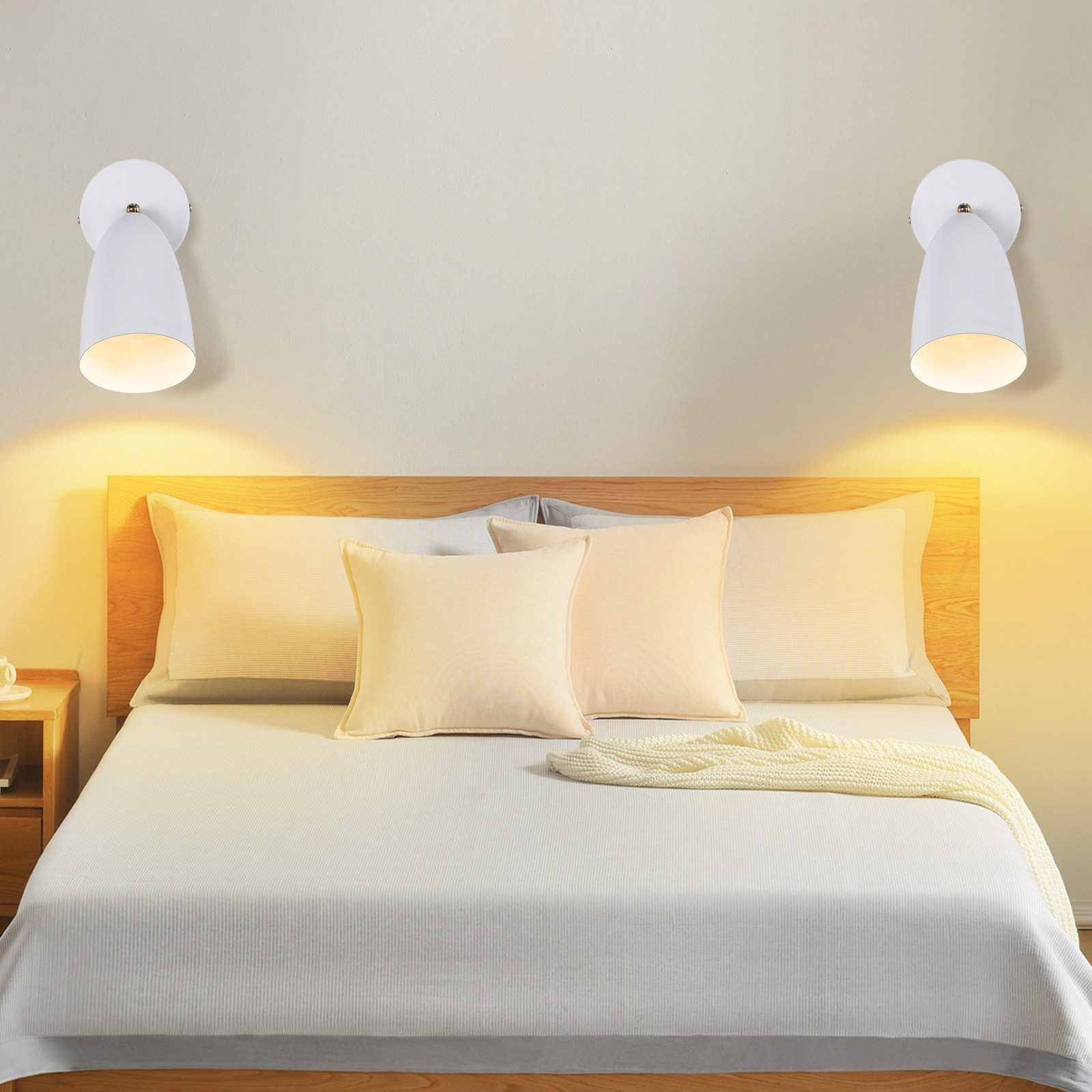 Due lampade da parete bianche sopra un letto, cuscini e una coperta.