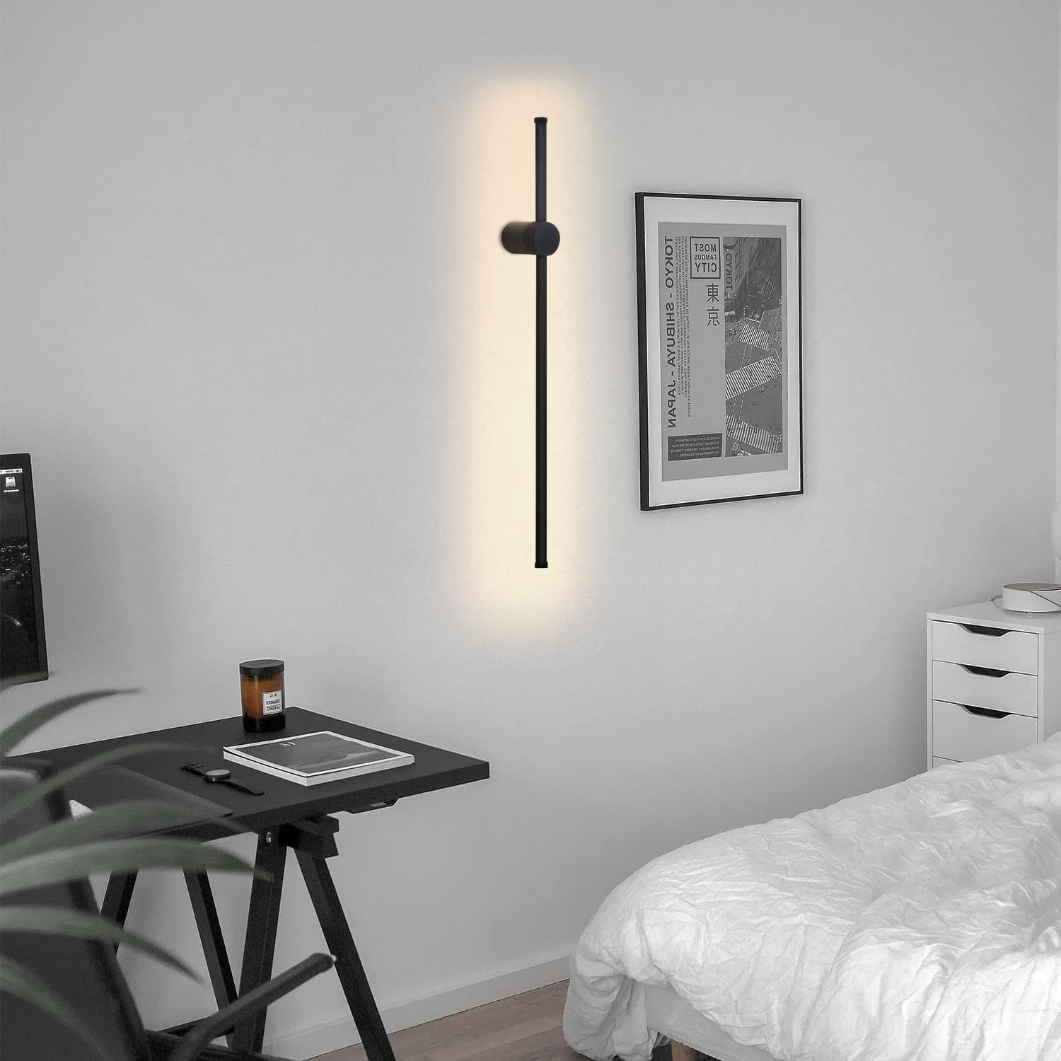 Un muro con un apparecchio di illuminazione nero. C'è anche un poster e un letto.
