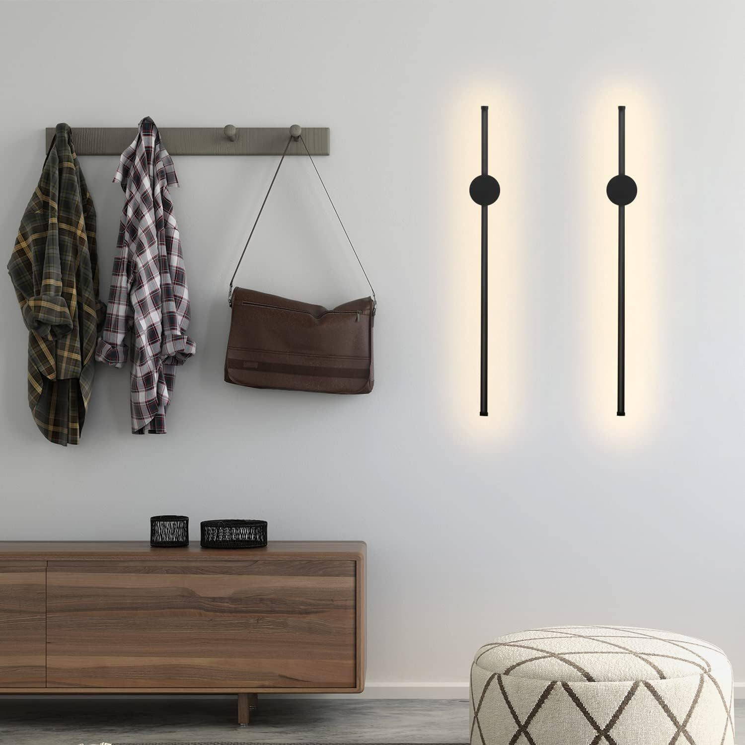 Due luci da parete nere con un cerchio in alto. Oggetti su un mobile in legno, con giacche e una borsa.