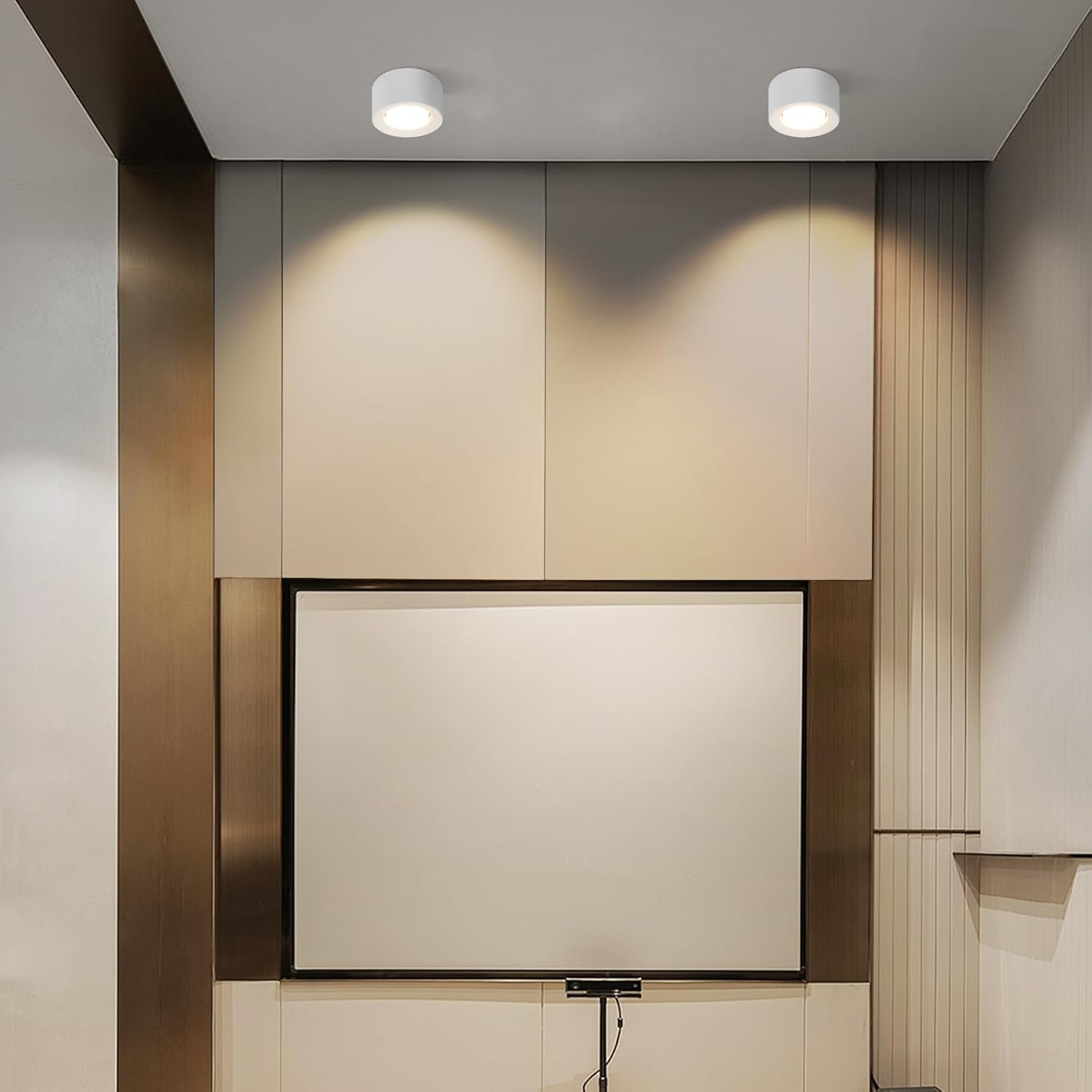Dos luces de techo redondas blancas iluminando una pared blanca con una pantalla grande.